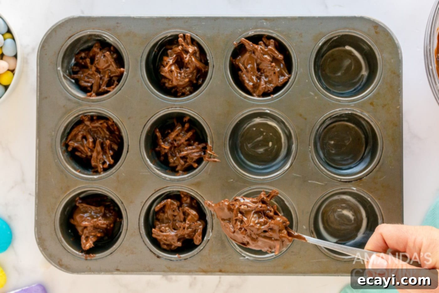 Nestled Treats 7 Spoonfuls of bird nest cookie mixture being placed into a buttered muffin pan, ready for shaping.