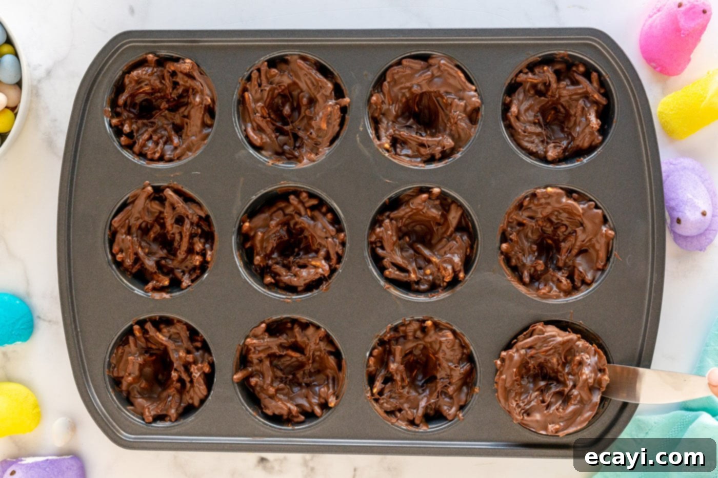 Nestled Treats 8 Bird nest cookie mixture in a muffin pan, with shallow wells pressed into the centers for candy eggs.