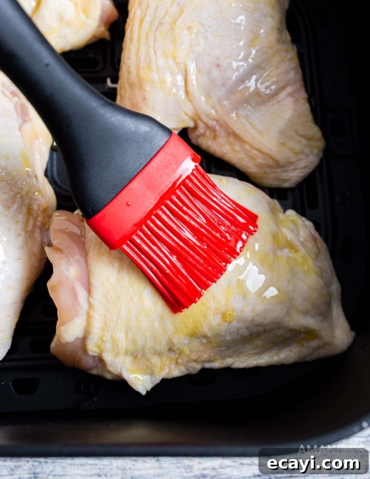 Crispy Air Fryer Chicken Thighs 6 A hand brushing olive oil onto a raw chicken thigh, preparing it for seasoning to ensure a crispy texture.