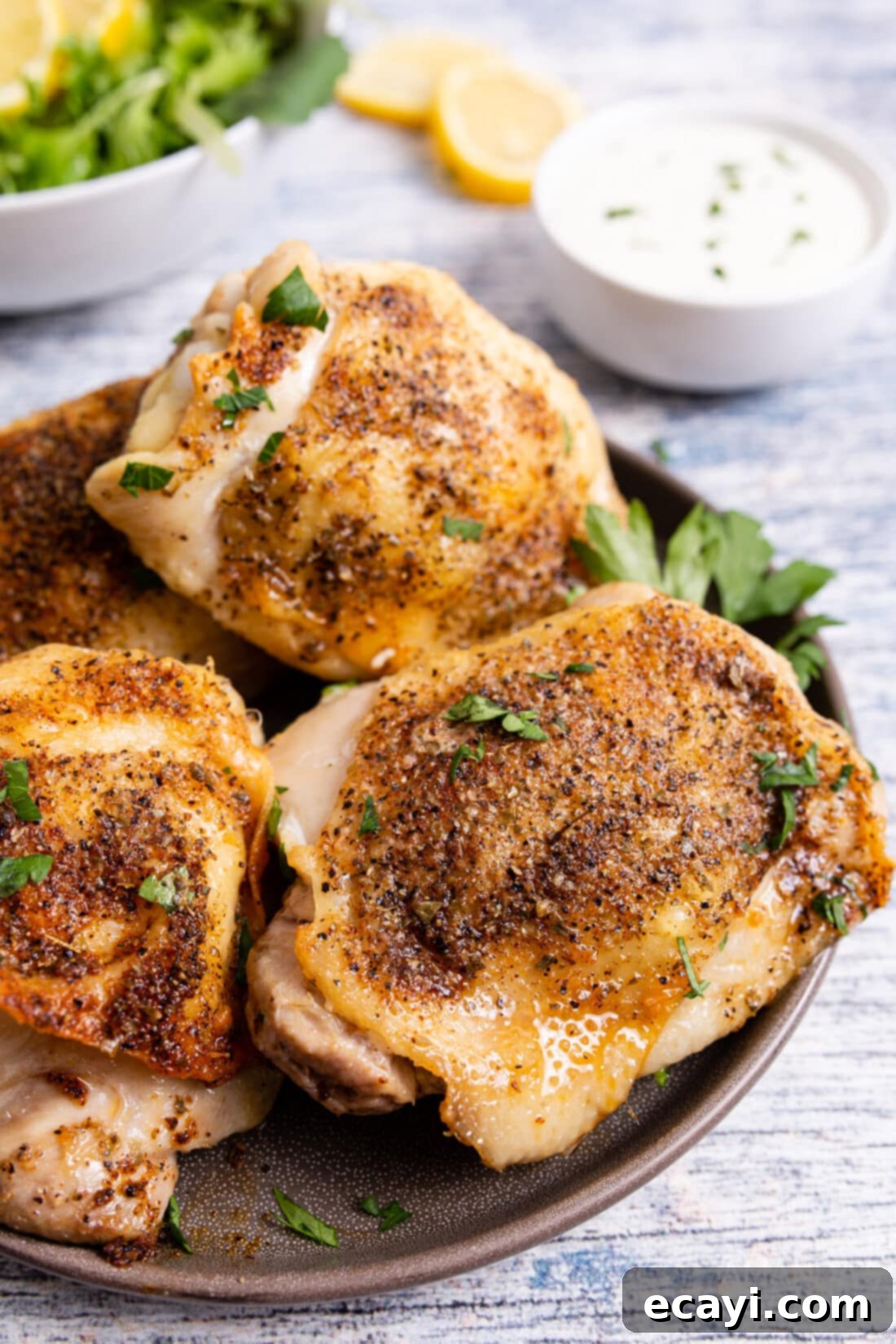 Crispy Air Fryer Chicken Thighs 9 Two air fried chicken thighs resting on a clean white plate, artfully garnished with fresh chopped parsley and a vibrant lemon wedge, ready to be served.