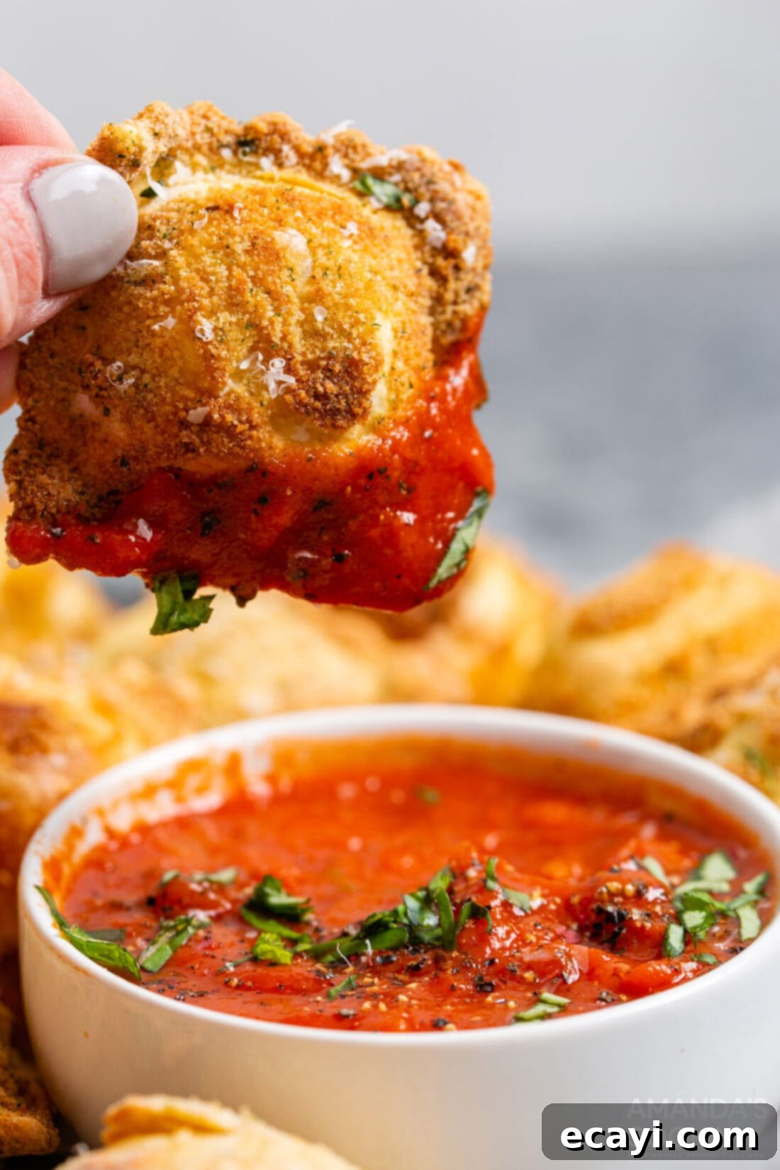 Crispy Air Fryer Ravioli 11 Hand dipping a piece of crispy air fryer ravioli into a bowl of marinara sauce