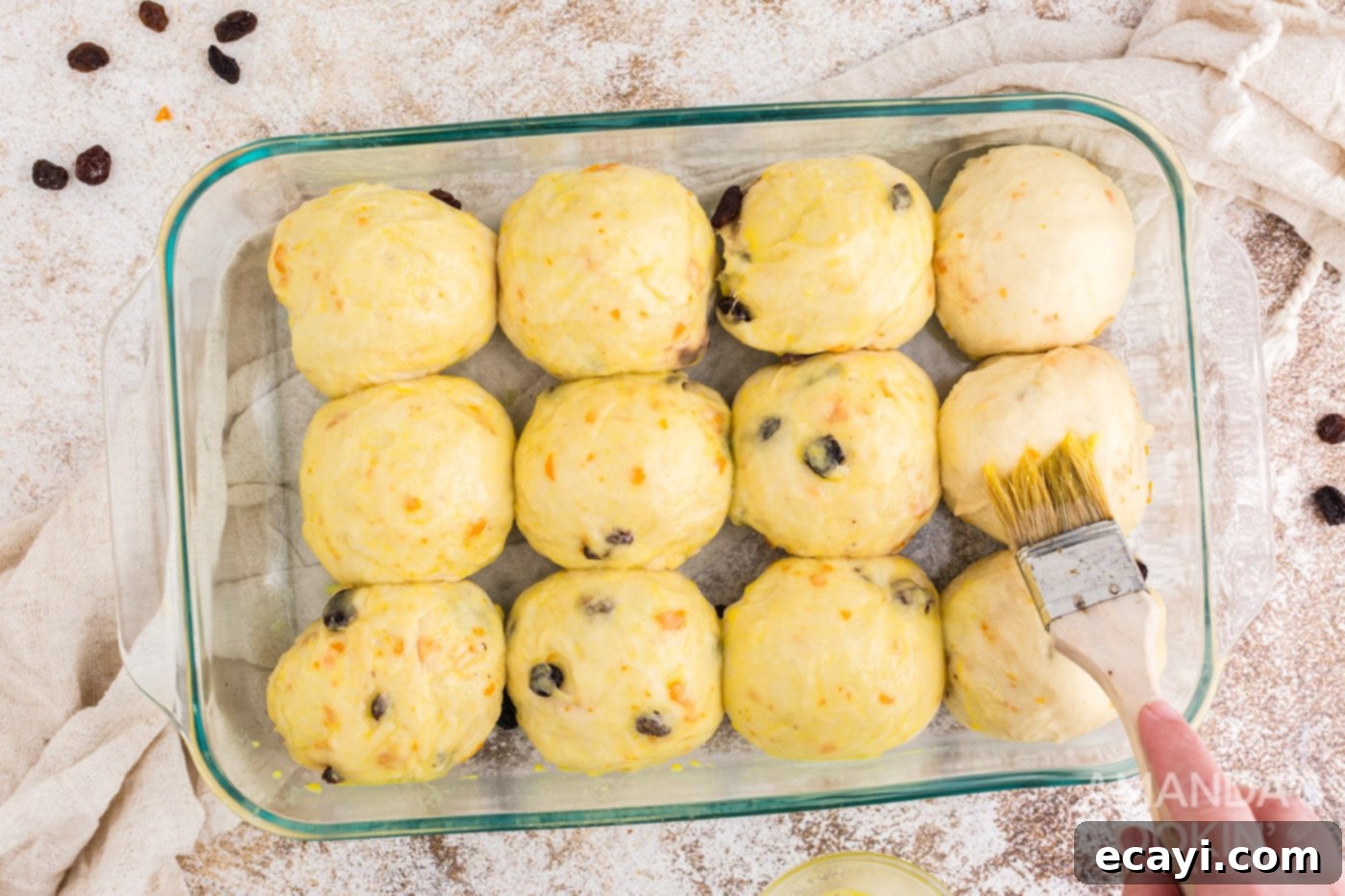 Spiced Easter Buns 16 Egg wash being brushed onto the tops of the risen dough balls in a baking dish before baking.