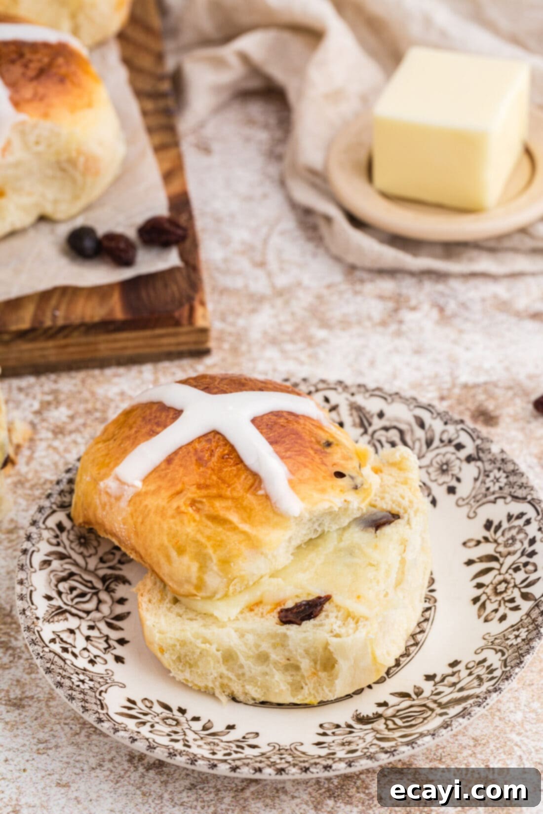 Spiced Easter Buns 18 A single Hot Cross Bun sliced in half on a white plate, revealing its soft interior and fruit pieces.