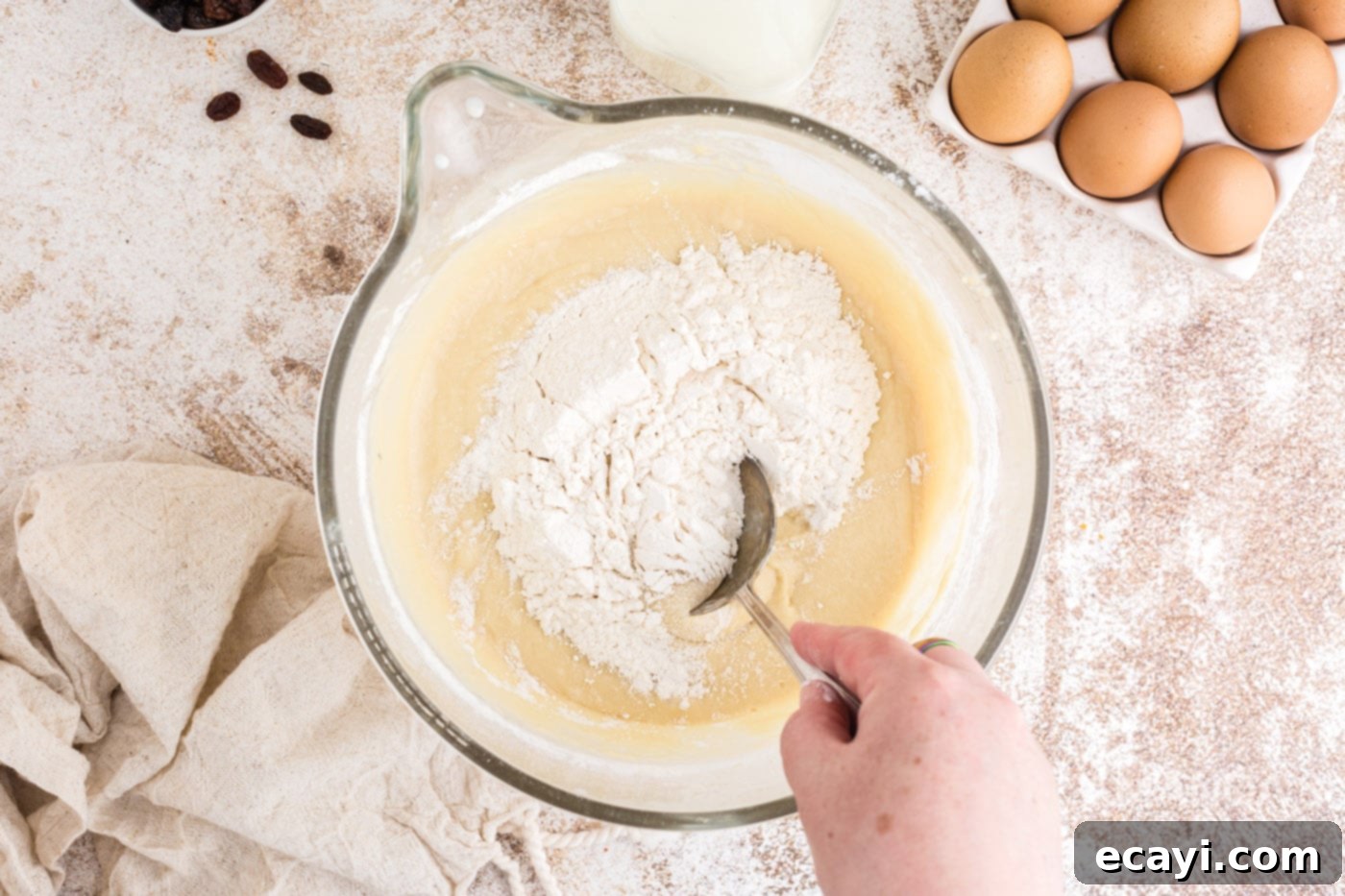 Spiced Easter Buns 9 A spoon stirring in additional flour into the dough in a mixing bowl to achieve a soft consistency.