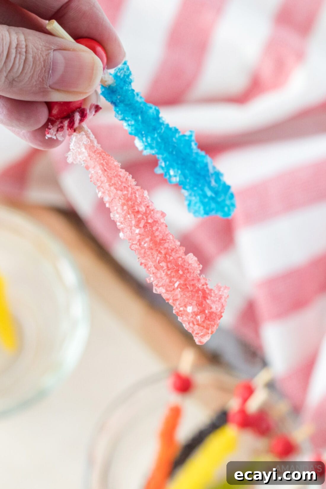 Edible Geodes 3 Hand holding two pieces of homemade rock candy on wooden sticks, showing clear and colored crystals