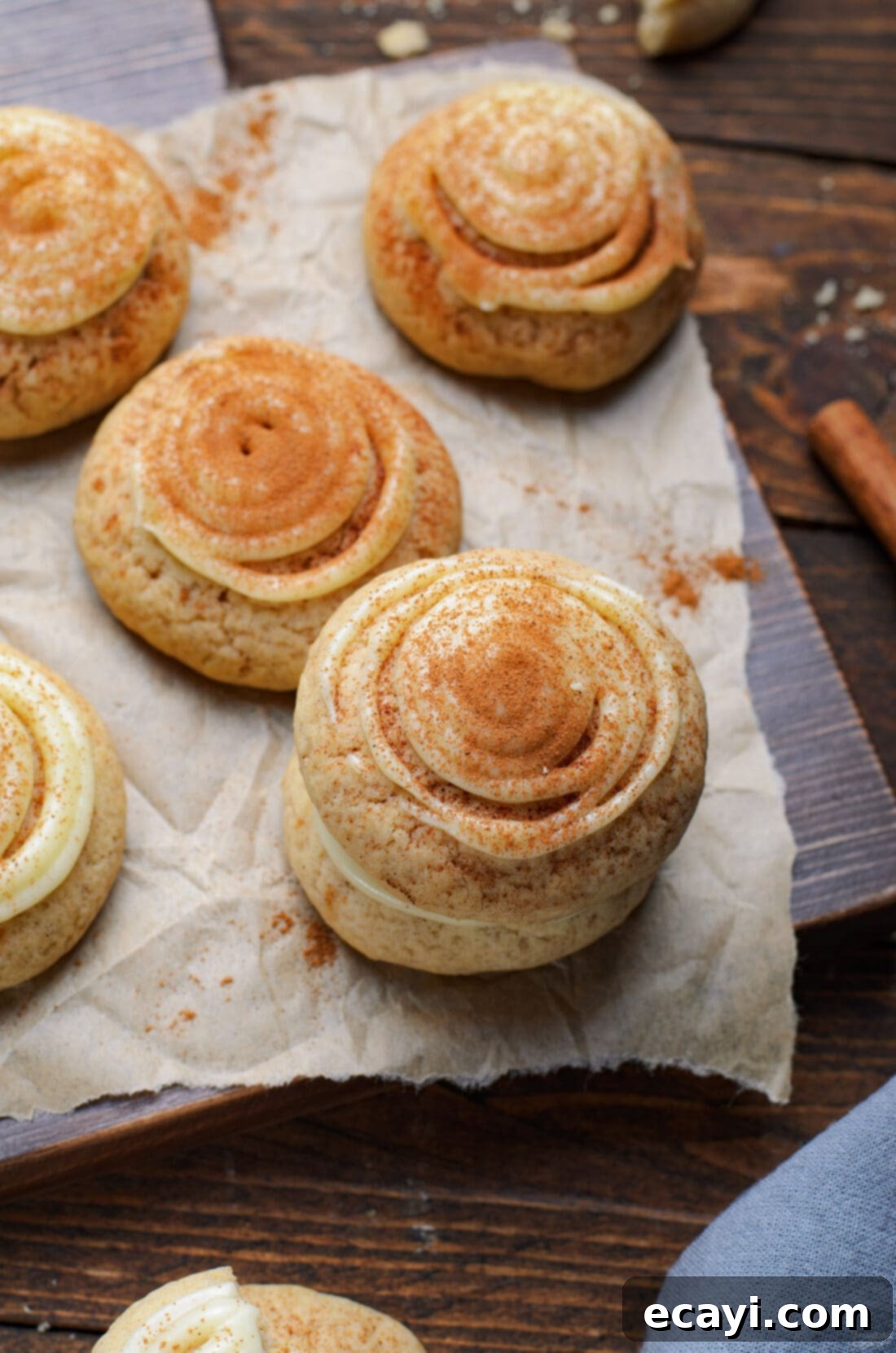 Cinnamon Swirl Delights 2 Soft and chewy cinnamon roll cookies topped with cream cheese frosting and cinnamon, laid out on parchment paper.