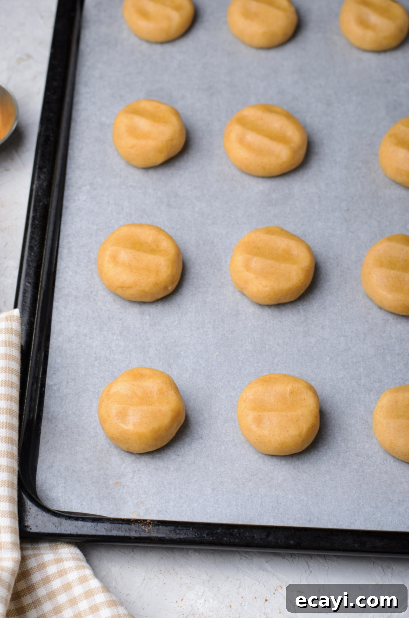Cinnamon Swirl Delights 8 Flattened balls of cinnamon roll cookie dough evenly spaced on a parchment-lined baking sheet, ready for the oven.