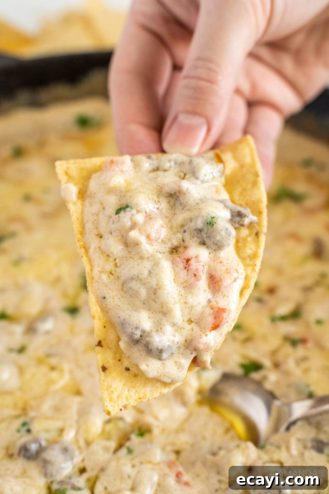 Loaded Philly Cheesesteak Dip 12 Lifting a generous scoop of hot, cheesy Philly Cheesesteak Dip with a tortilla chip.