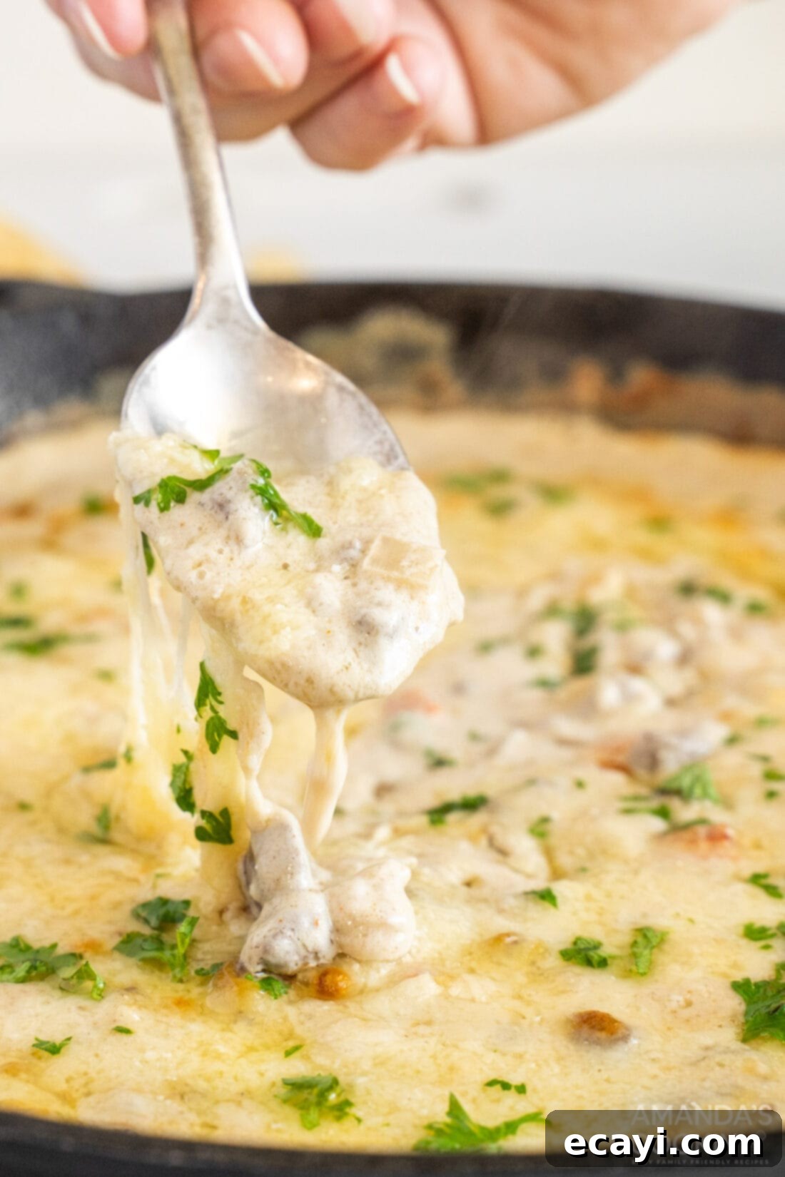 Loaded Philly Cheesesteak Dip 3 Lifting a spoonful of hot, gooey Philly Cheesesteak Dip from a skillet.