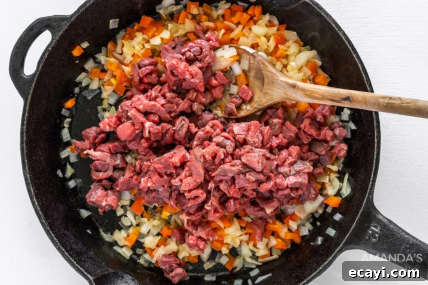 Loaded Philly Cheesesteak Dip 7 Chopped steak browning on top of sautéed vegetables in a cast iron skillet.