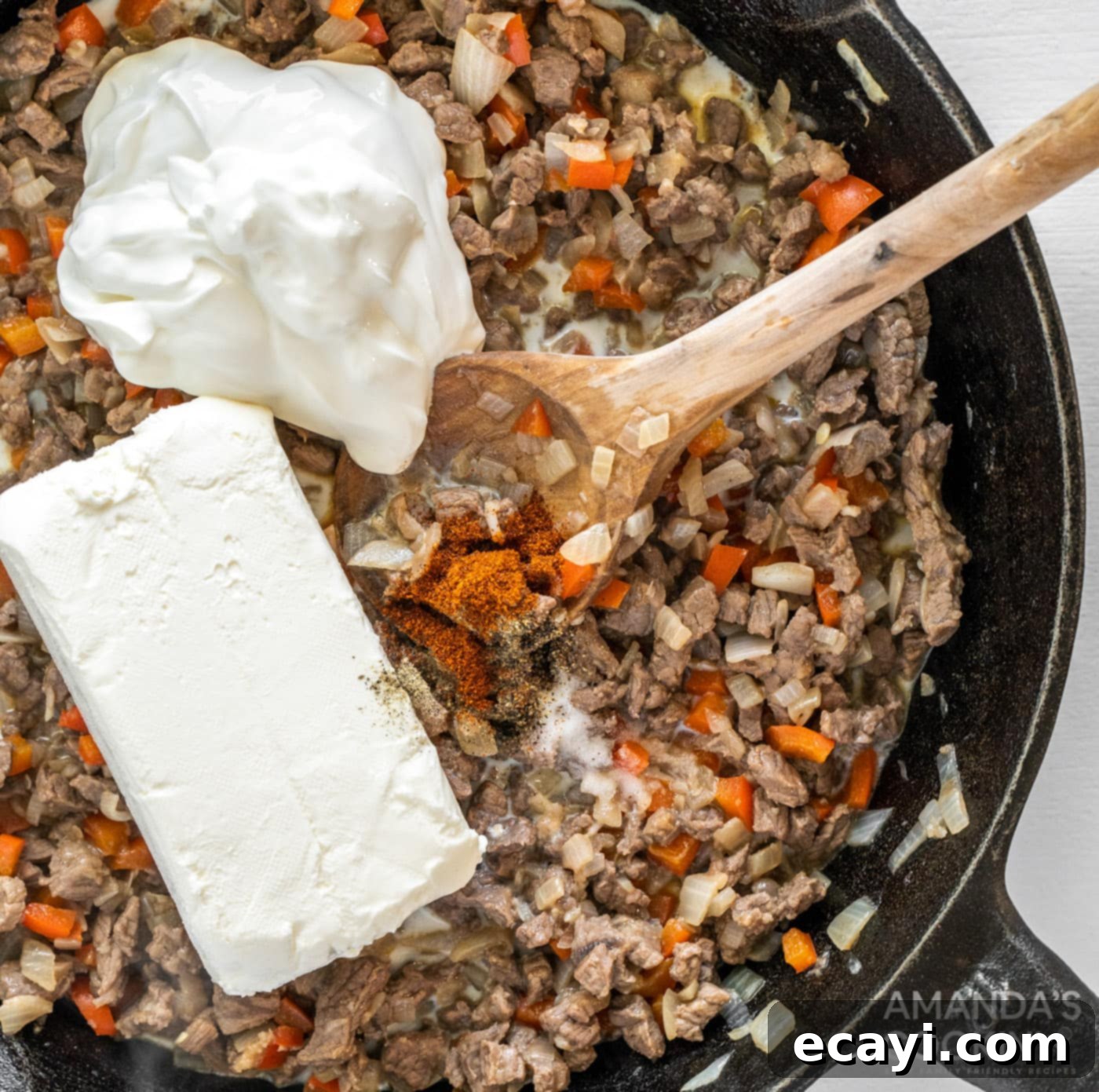 Loaded Philly Cheesesteak Dip 9 Sour cream and cream cheese being added to the cooked meat and vegetable mixture in a skillet.