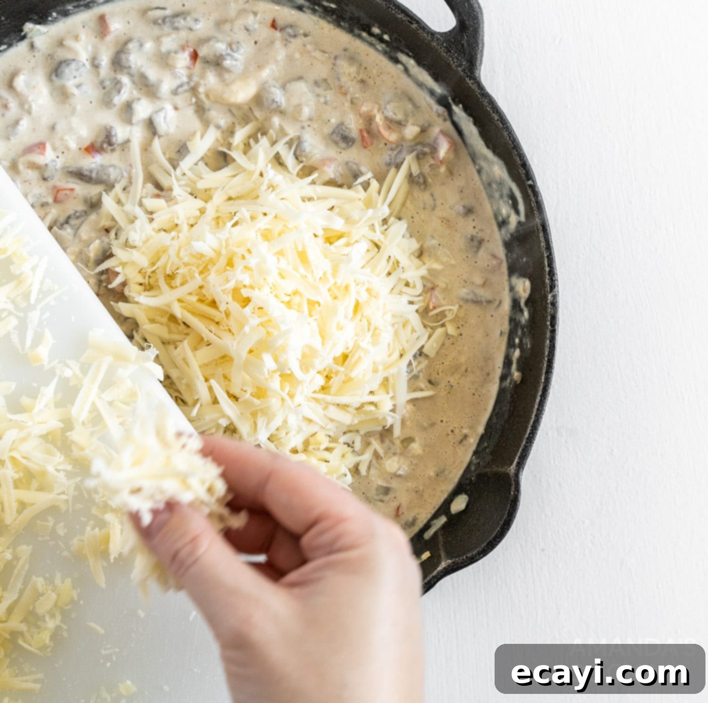 Loaded Philly Cheesesteak Dip 10 Shredded provolone cheese being stirred into the creamy meat and vegetable mixture in a skillet.