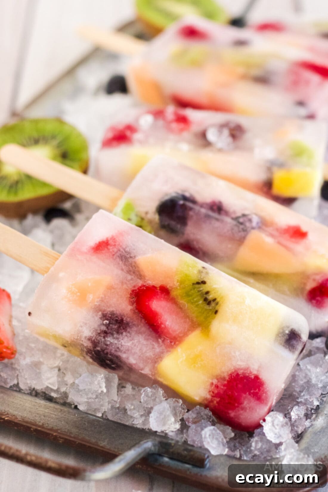 Refreshing Fruit Treats 2 Vibrant homemade fruit popsicles displayed artfully on a tray of ice cubes, featuring colorful layers of berries, kiwi, and pineapple.