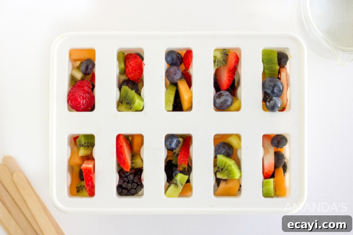 Refreshing Fruit Treats 5 Chopped fresh fruits like berries, kiwi, and pineapple being carefully placed into clear popsicle molds for homemade fruit popsicles.
