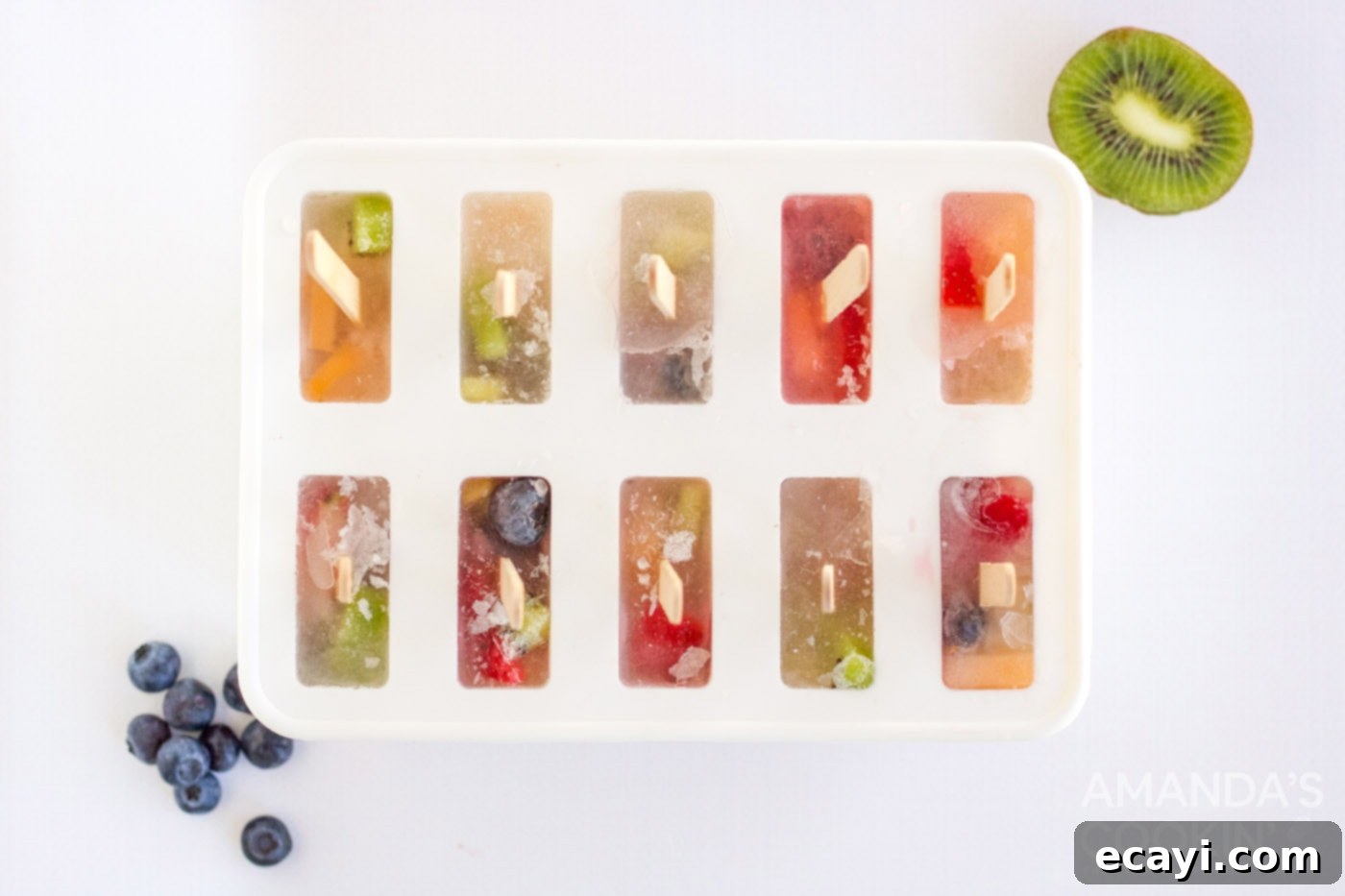 Refreshing Fruit Treats 7 A row of perfectly frozen homemade fruit popsicles still in their molds, showcasing the vibrant fruit pieces suspended within the ice.