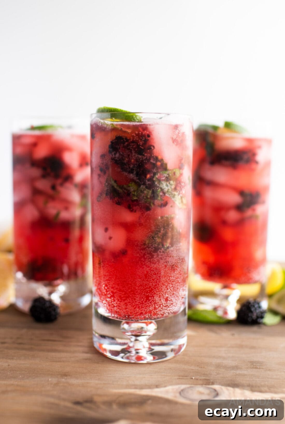 Midnight Berry Mojito 2 Three elegant glasses of sparkling Blackberry Mojito garnished with fresh fruit and mint, perfect for a summer gathering