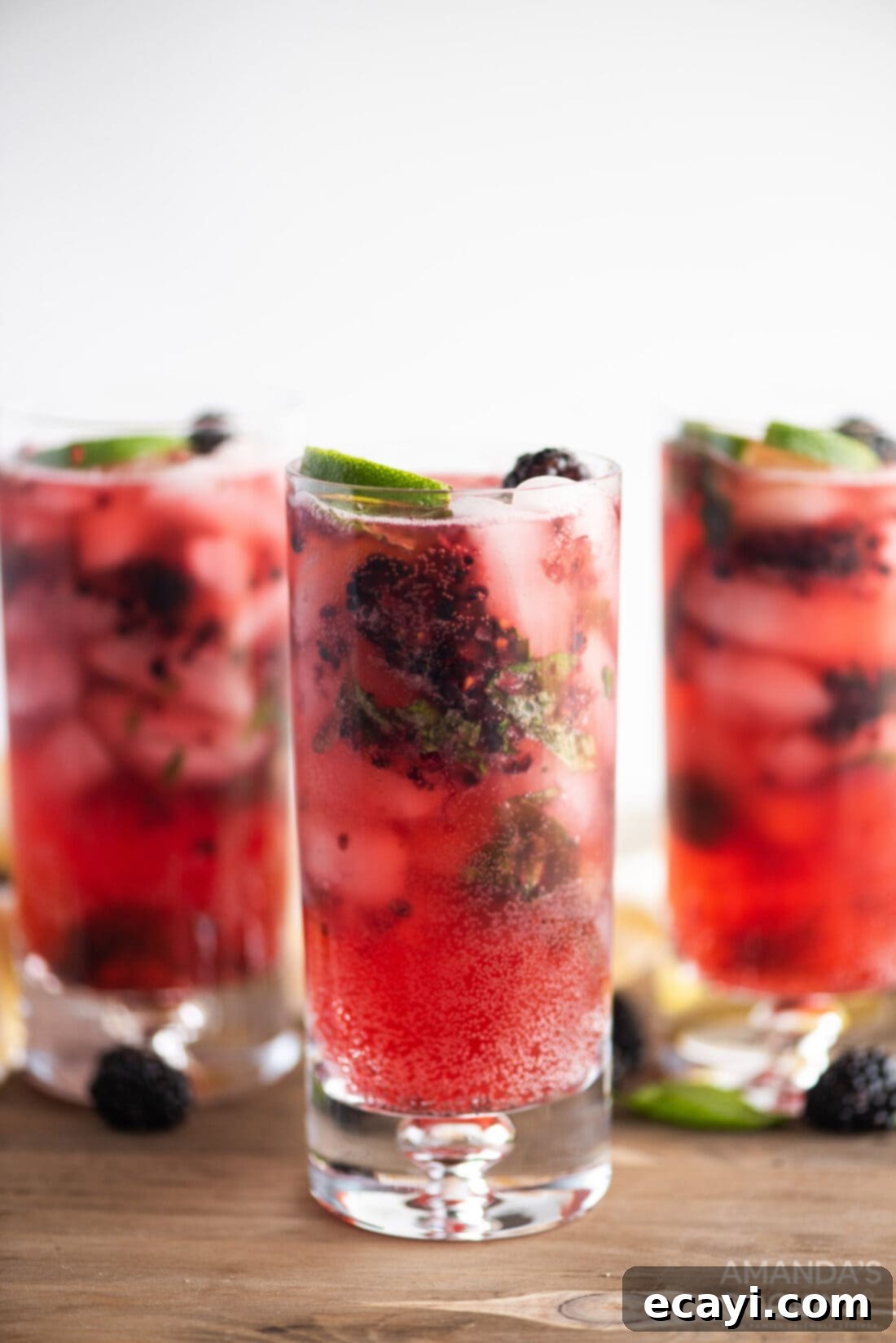 Midnight Berry Mojito 8 Three blackberry mojito cocktails arranged on a wooden surface, showcasing their vibrant color and fresh garnishes