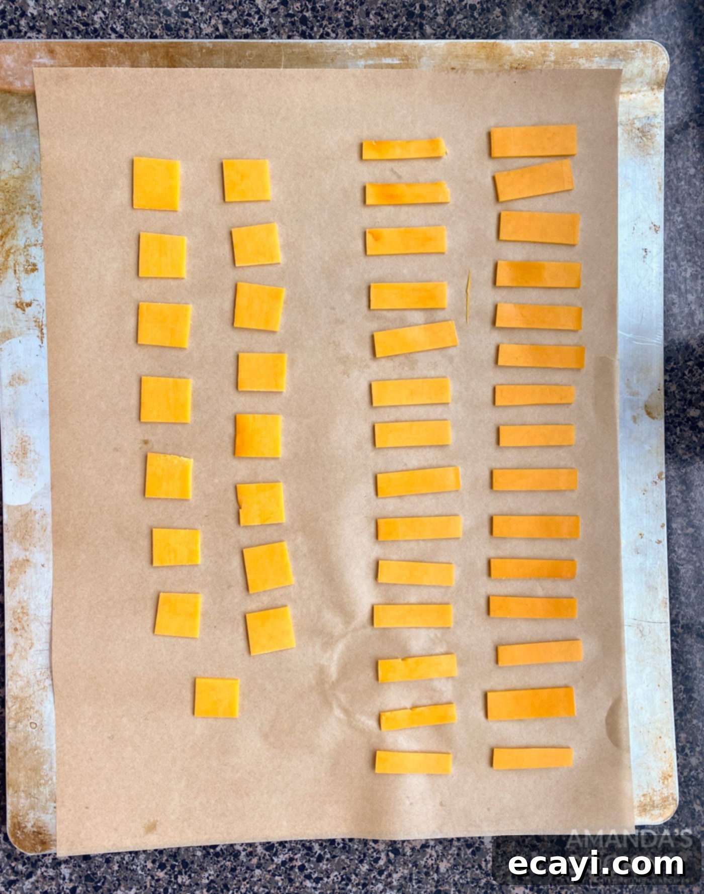 Crunchy Keto Cheese Bites 5 Evenly cut small squares of cheddar cheese arranged on a parchment-lined baking sheet, spaced out for baking.