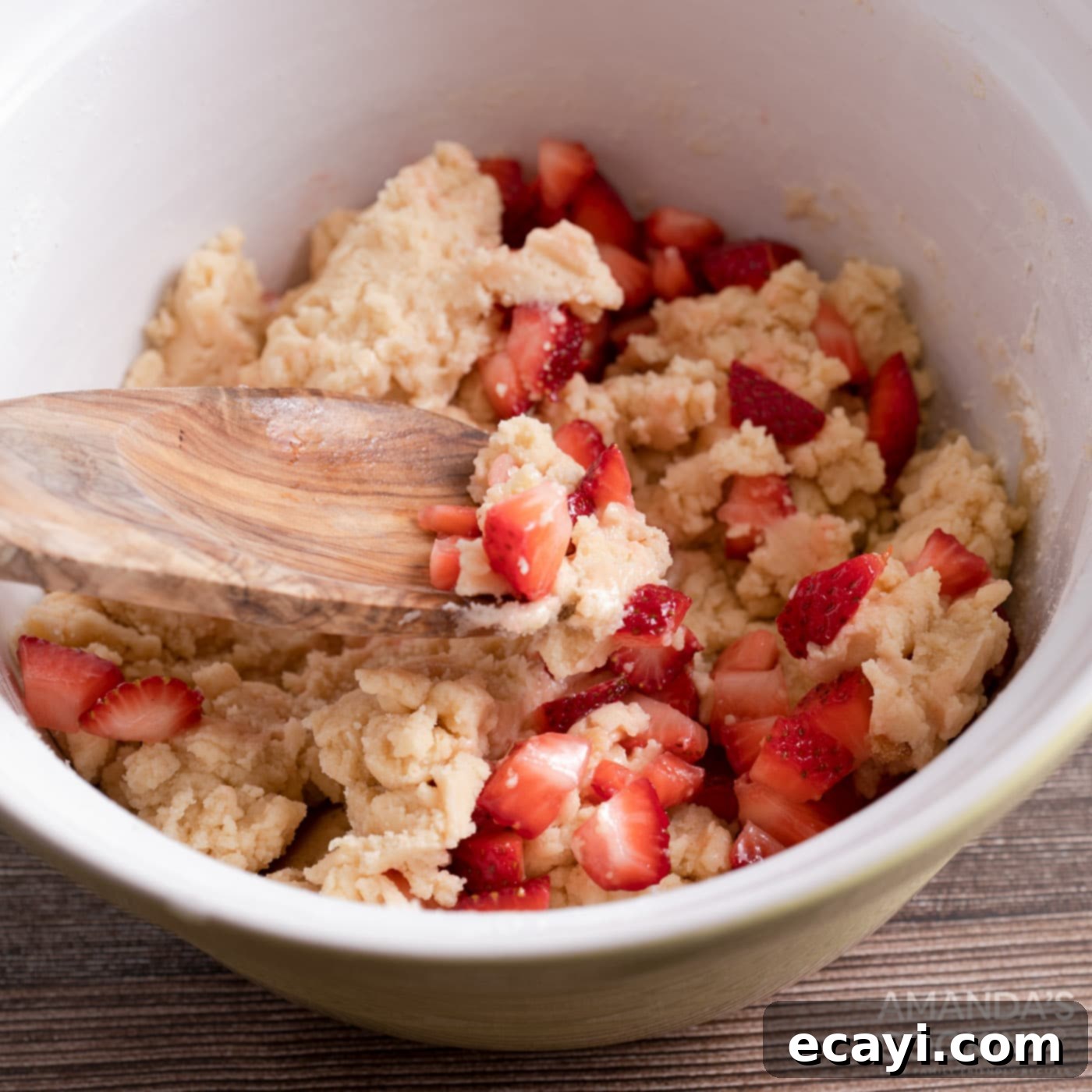 Zesty Strawberry Lemonade Cookies 7 A wooden spoon gently folding macerated strawberries into a bowl of cookie dough.
