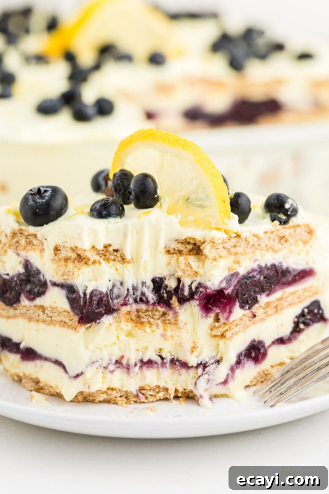 Zesty Lemon Blueberry Cloud Cake 2 A vibrant slice of Lemon Blueberry Icebox Cake with a bite taken out, showing distinct layers of lemon pudding, blueberry filling, and graham crackers.