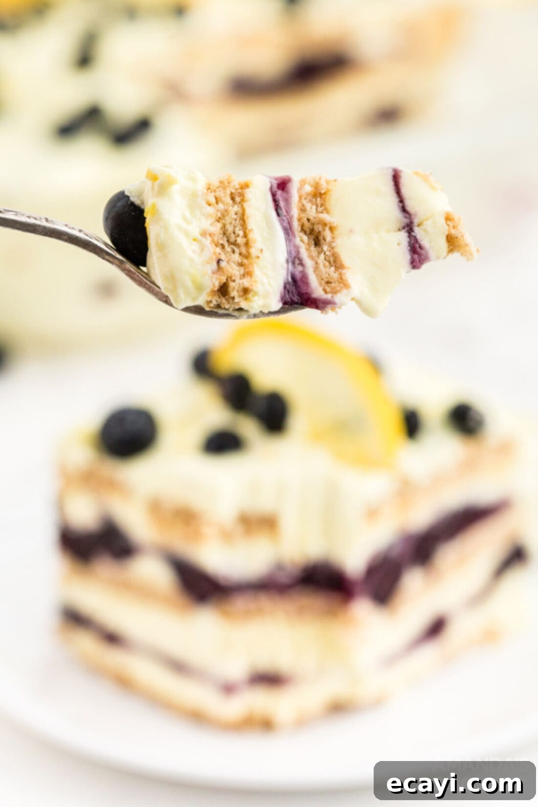 Zesty Lemon Blueberry Cloud Cake 13 A fork taking a bite from a slice of Lemon Blueberry Icebox Cake, highlighting the creamy texture.