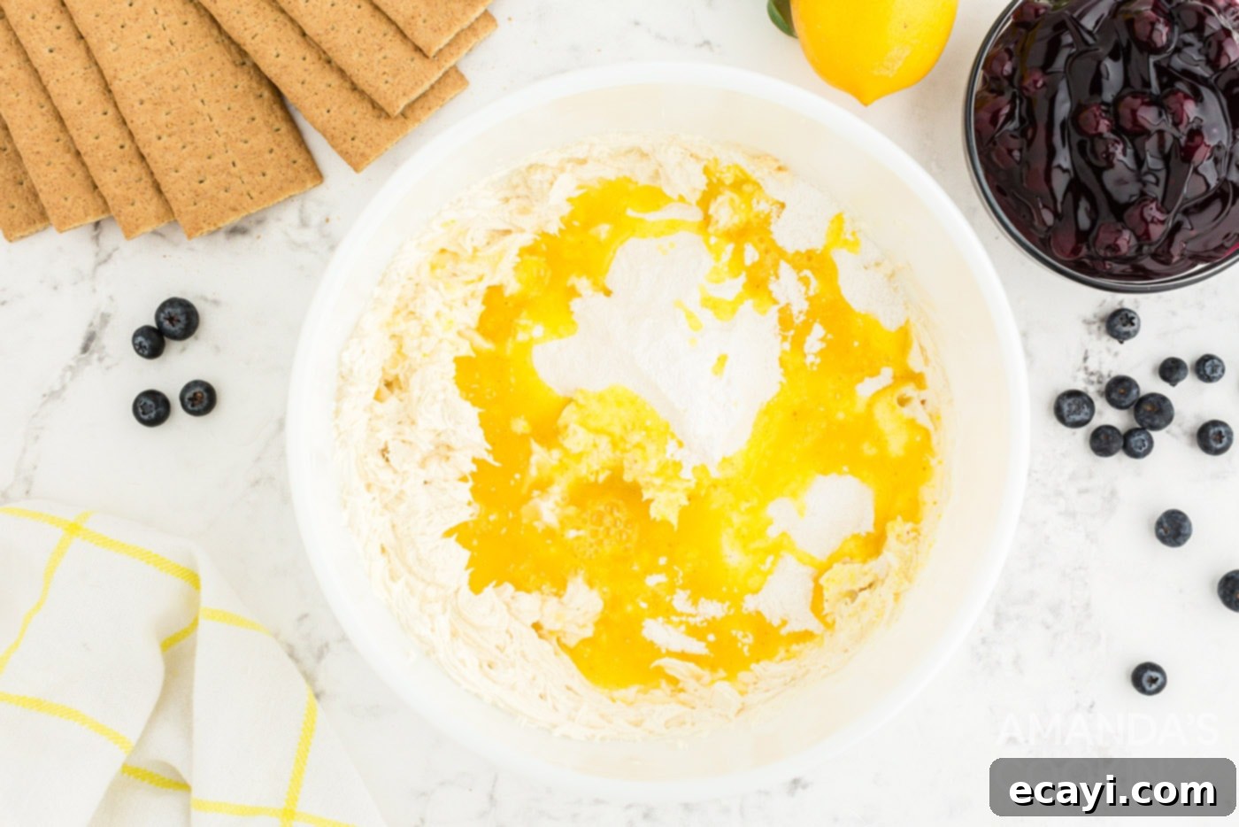 Zesty Lemon Blueberry Cloud Cake 5 Mixing instant pudding, lemon juice, vanilla extract, and milk into cream cheese in a bowl.