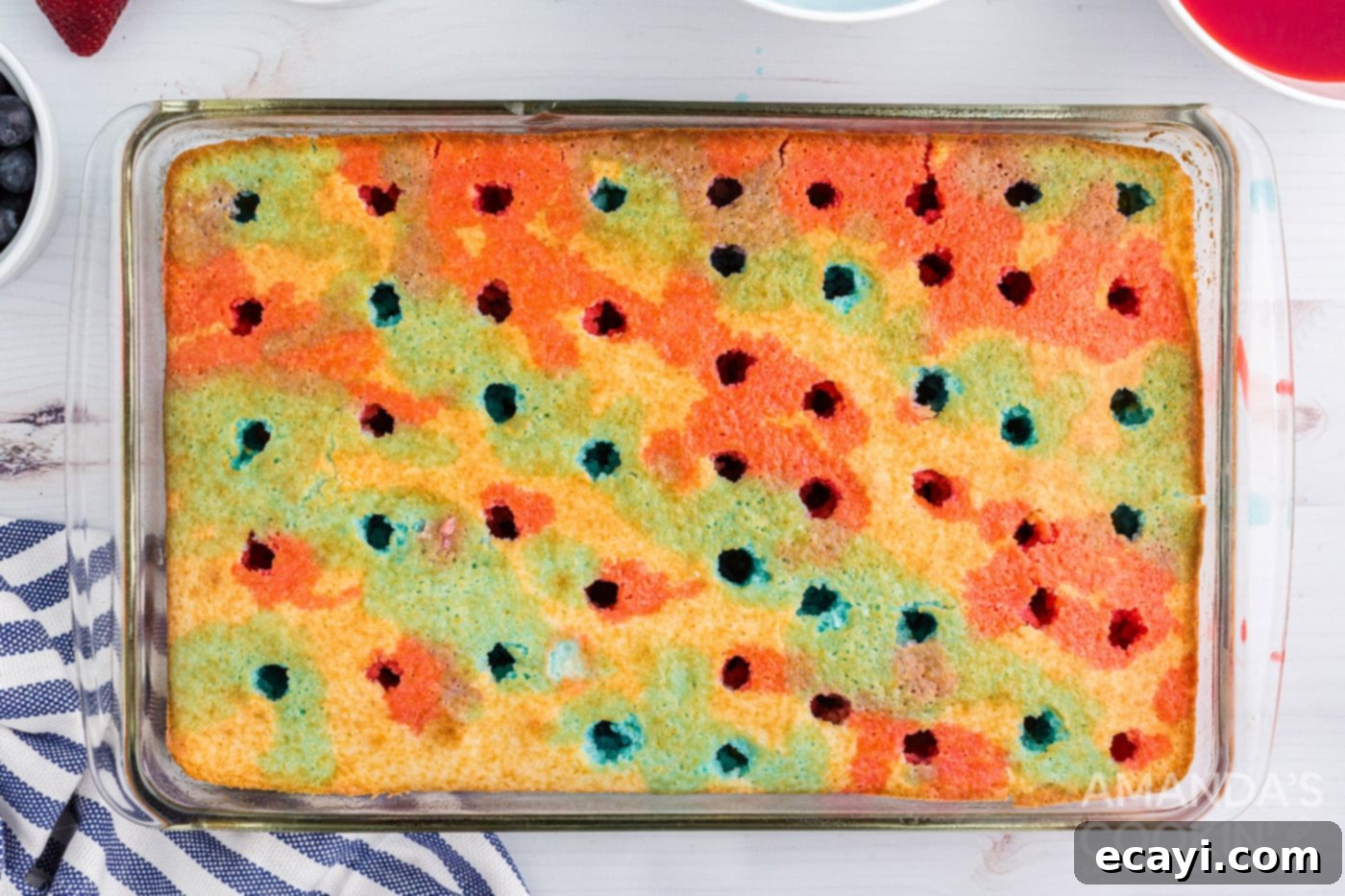 Patriotic Red, White and Blue Poke Cake 7 Blue and red jello being drizzled in alternating rows over a white cake with holes, creating a colorful pattern.