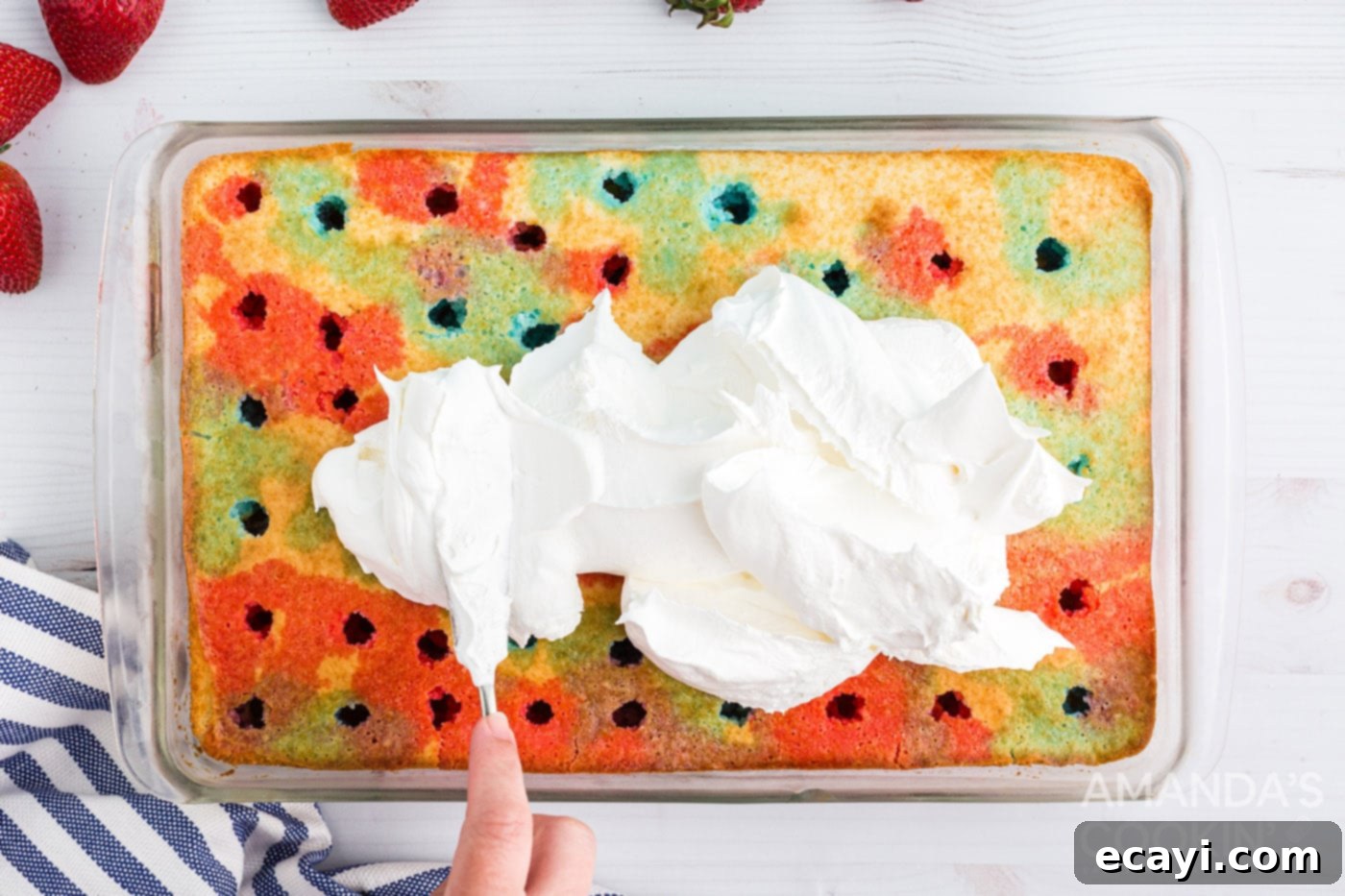 Patriotic Red, White and Blue Poke Cake 8 A hand smoothly spreading a layer of white Cool Whip over the top of a Jell-O infused poke cake.