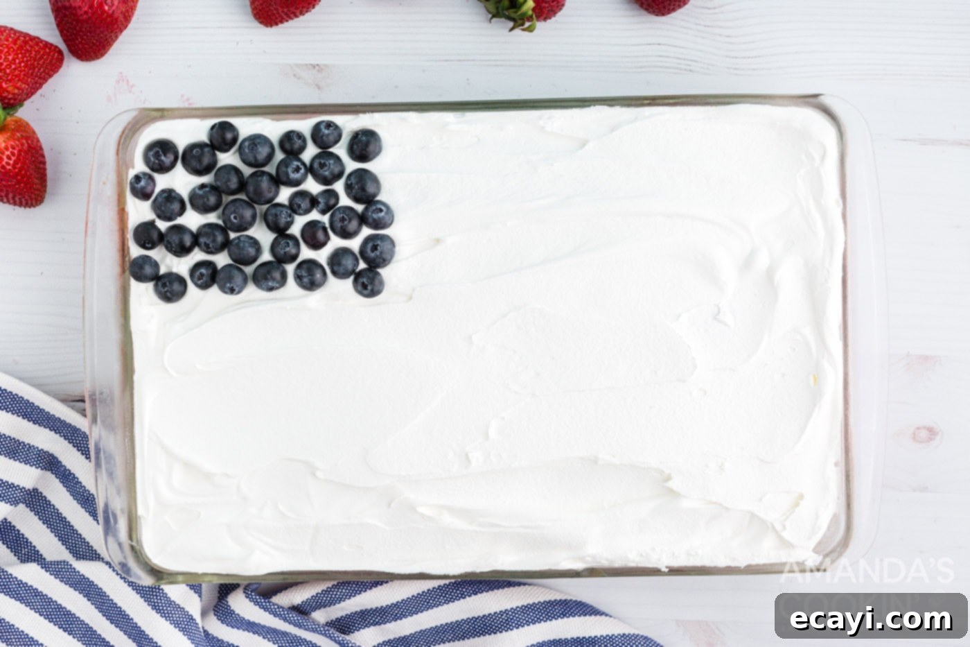 Patriotic Red, White and Blue Poke Cake 9 Fresh blueberries arranged in the top left corner of a white frosted cake, forming part of an American flag design.