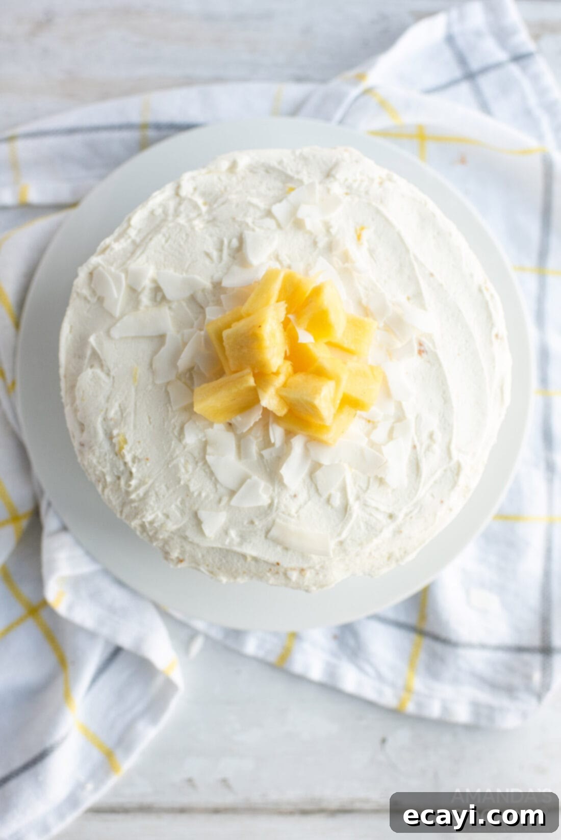Golden Pineapple Bliss 3 Overhead view of a beautifully frosted Pineapple Cake with a sprinkle of shredded coconut on top.