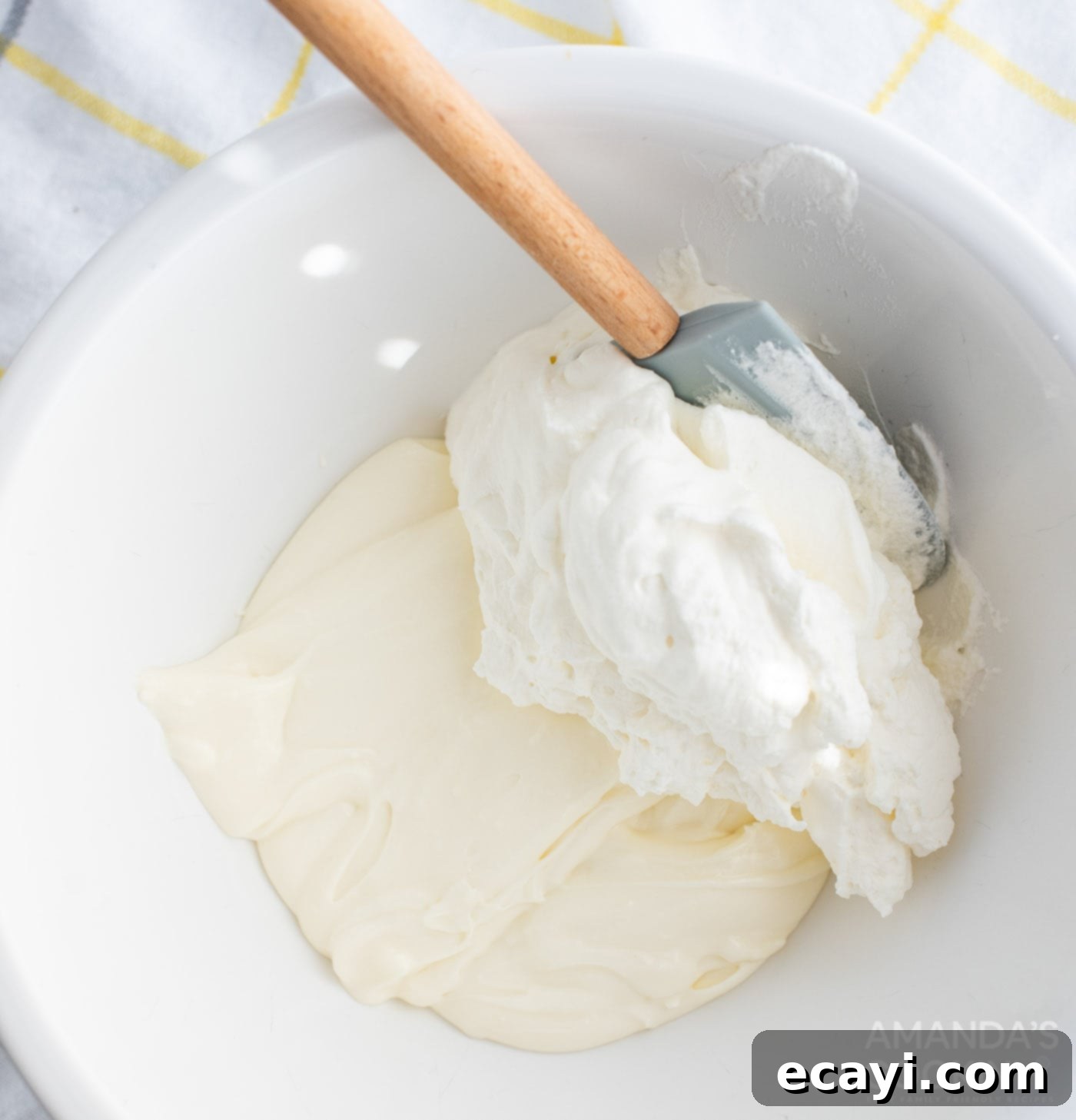 Golden Pineapple Bliss 6 A spatula gently folding whipped cream into a creamy cream cheese mixture for the cake filling.