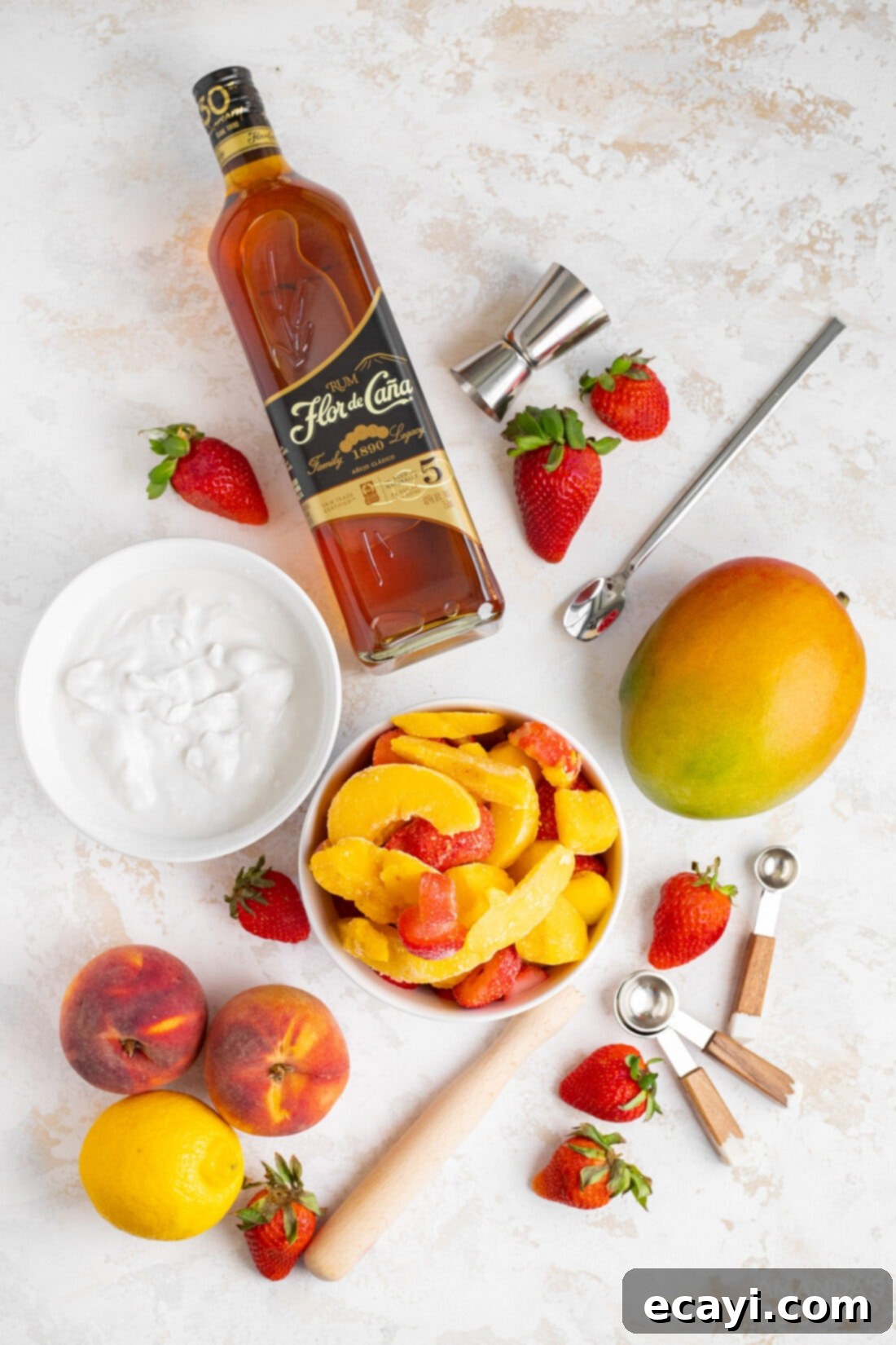 Island Vibes Rum Slush 4 An appetizing overhead shot of fresh and frozen ingredients laid out for Tropical Rum Slush, including peaches, mangoes, strawberries, coconut cream, rum, and a lemon.