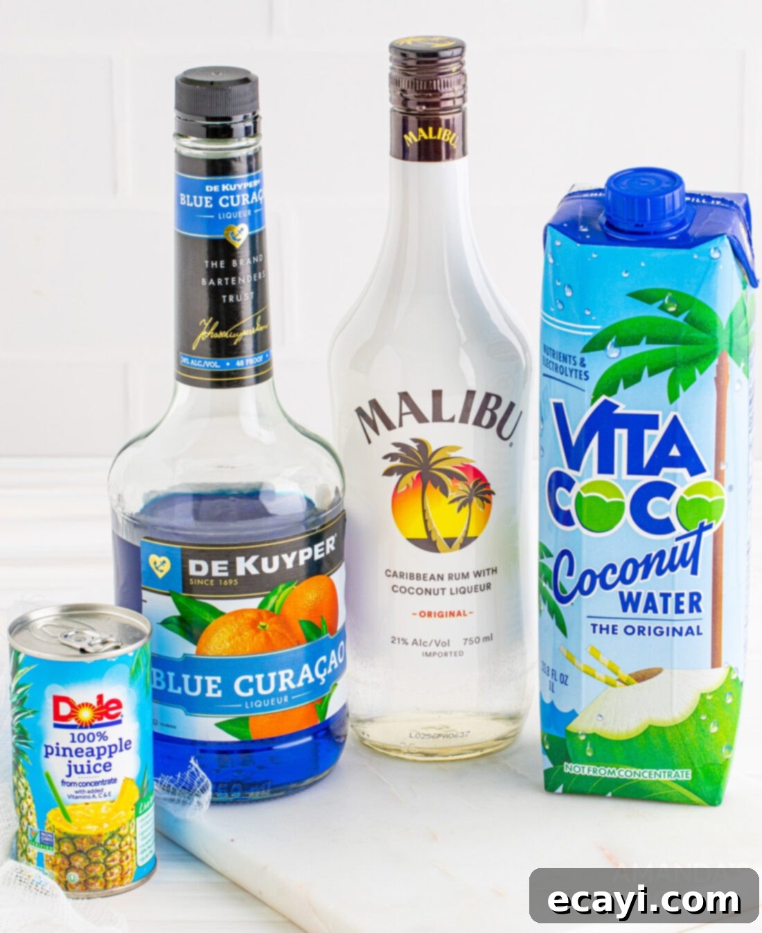 Sapphire Sea Sip 4 Ingredients laid out for making an Ocean Water Cocktail: blue curacao, coconut rum, pineapple juice, and coconut water.