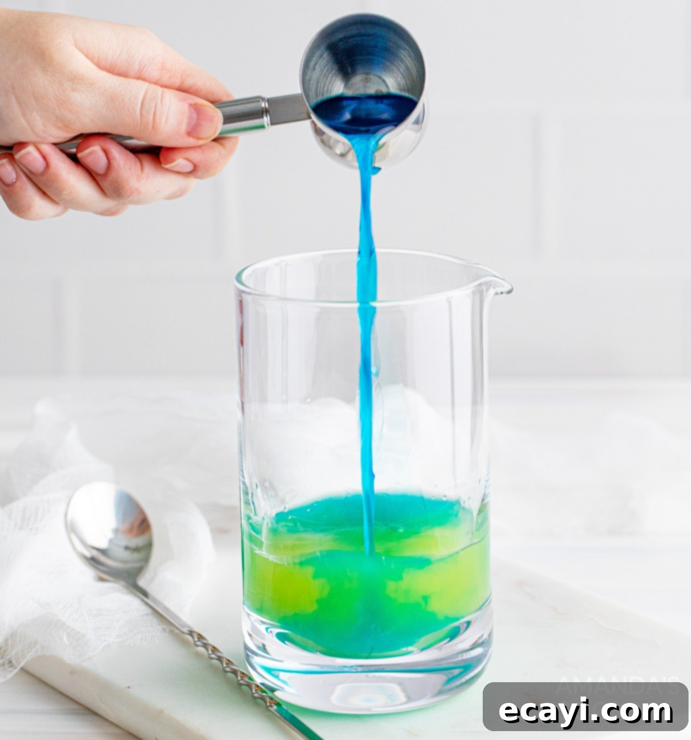 Sapphire Sea Sip 6 Pouring blue curacao into a cocktail mixing glass with other ingredients.