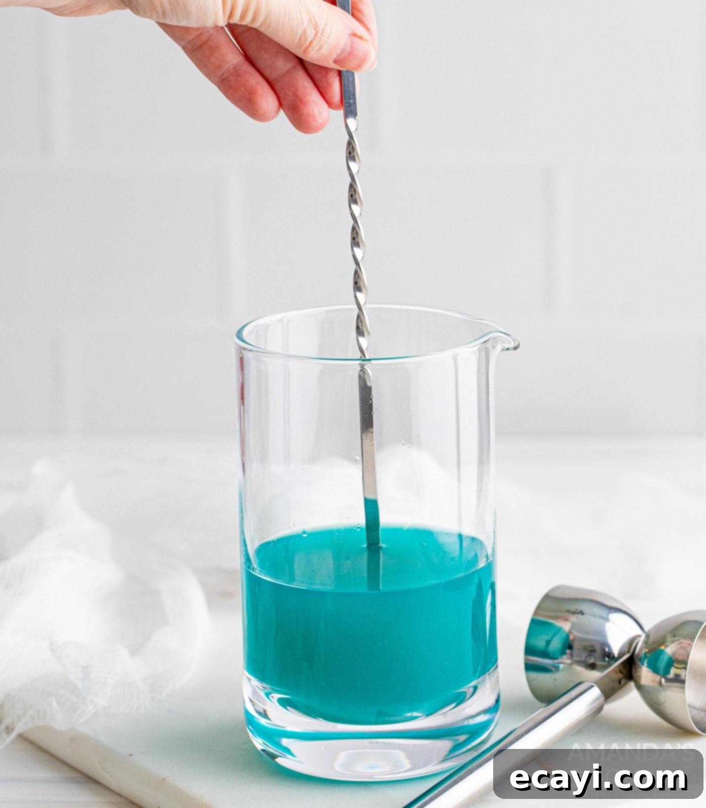 Sapphire Sea Sip 7 Stirring the cocktail ingredients in a mixing glass with a bar spoon.