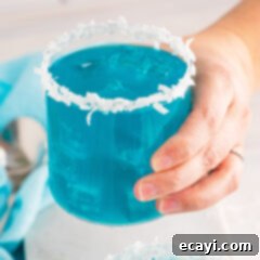 Sapphire Sea Sip 10 A close-up of a hand holding a glass of the blue Ocean Water Cocktail, with a blurred background.