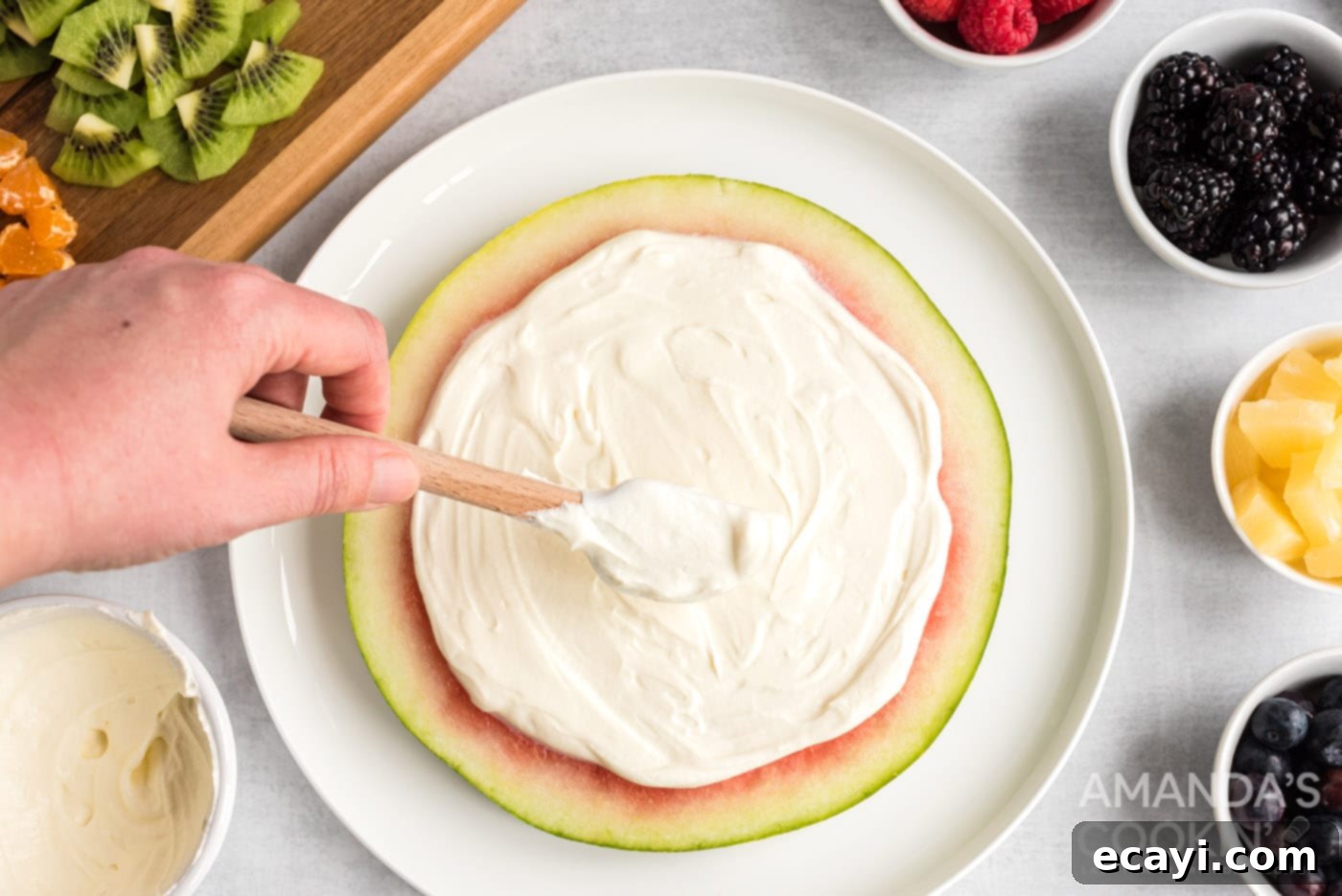 Watermelon Wonder Wheels 10 A rubber spatula smoothly spreading the white cream cheese and yogurt mixture over a round watermelon slice.