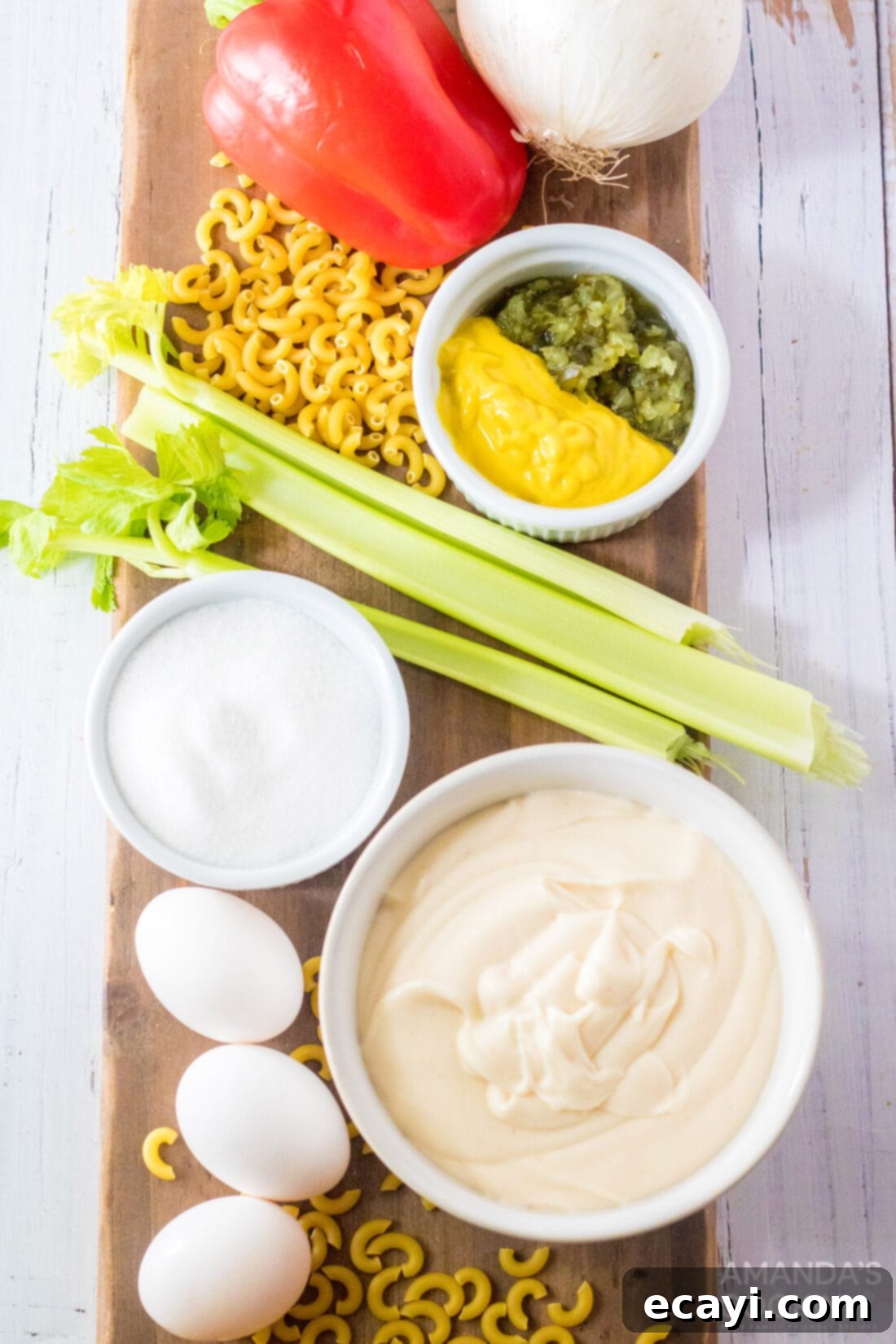 Creamy Amish Macaroni Perfection 4 A clear glass bowl filled with all the fresh ingredients needed for Amish Macaroni Salad: macaroni, hard-boiled eggs, celery, red bell pepper, onion, and sweet pickle relish, awaiting assembly.