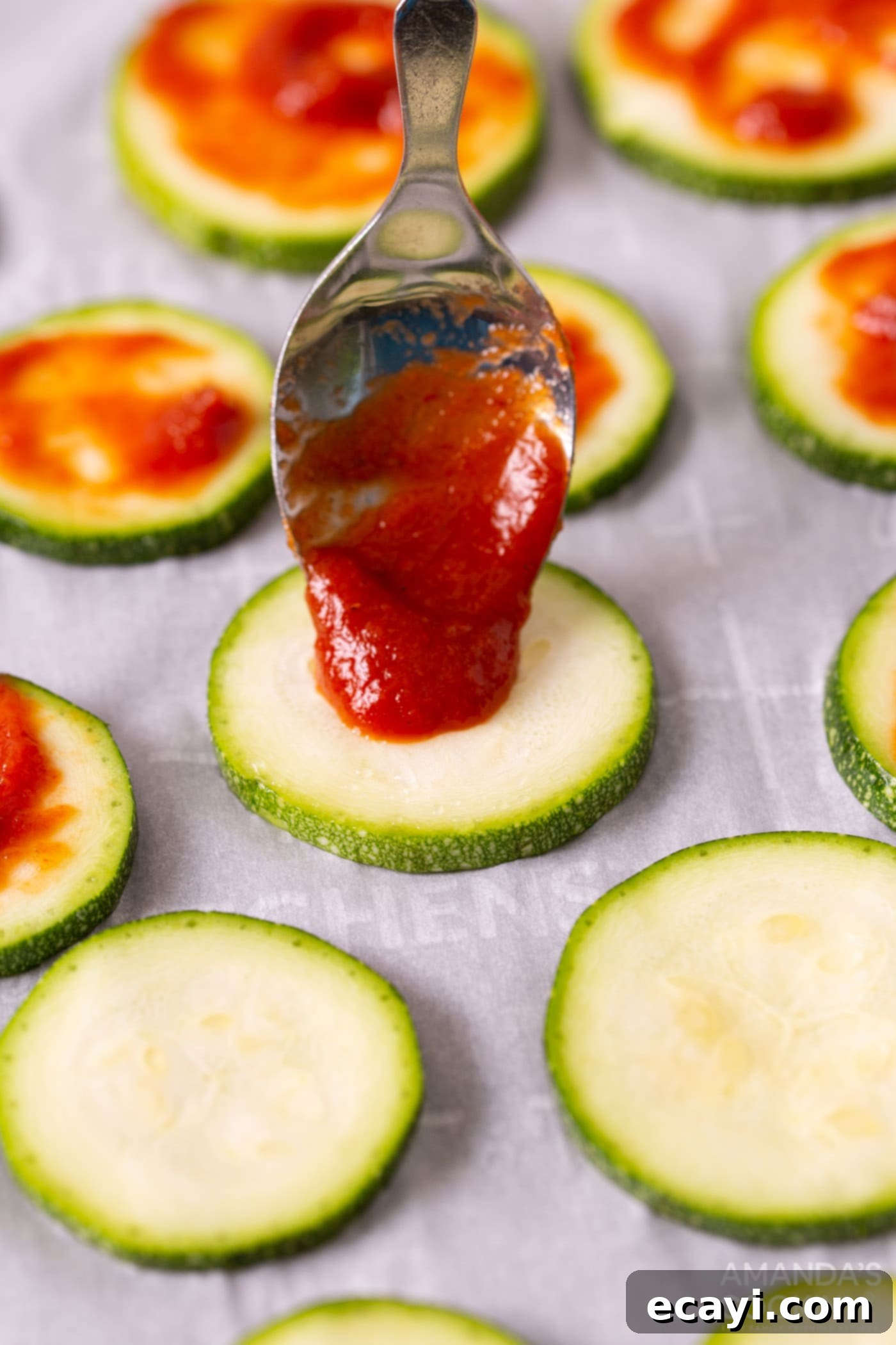 Zucchini Pizza Bites 6 spoon pouring pizza sauce onto zucchini slice