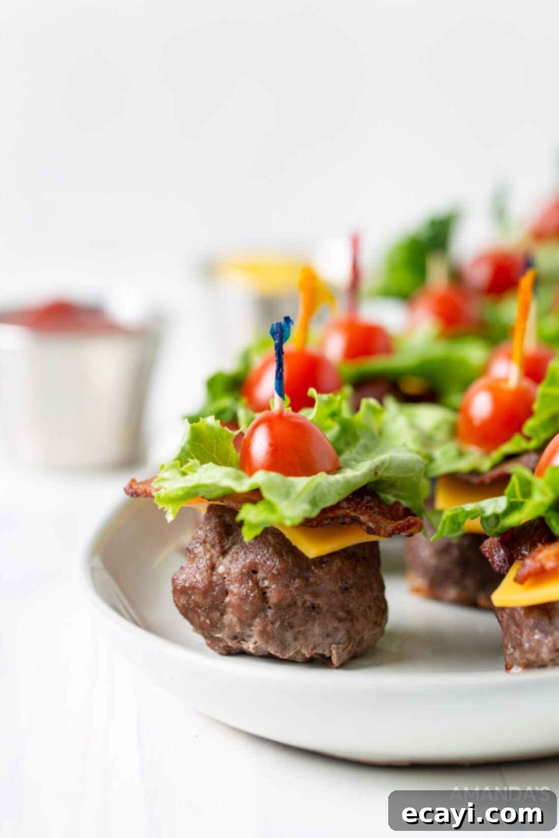 Mini Bacon Cheeseburger Poppers 2 A plate brimming with neatly arranged Bacon Cheeseburger Meatballs, each topped with cheese, bacon, lettuce, and a cherry tomato, ready to be served at a party or tailgating event.