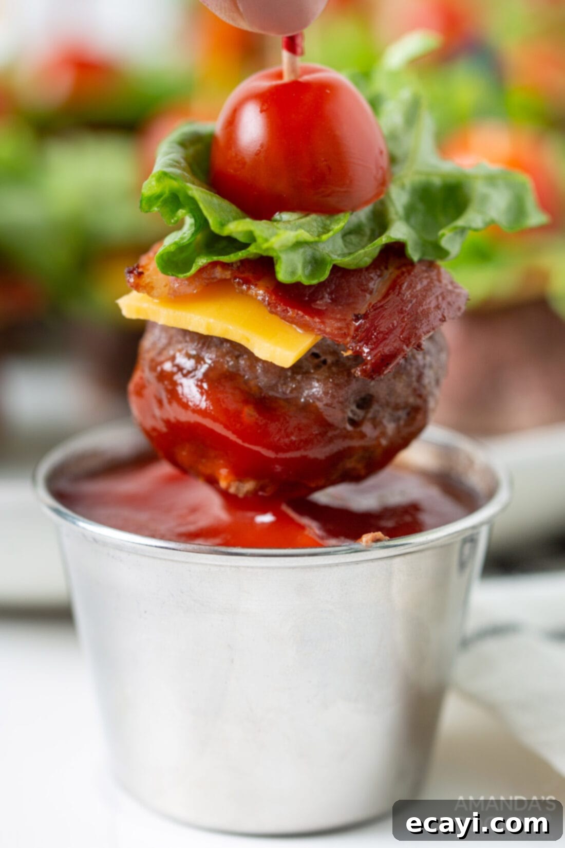 Mini Bacon Cheeseburger Poppers 3 A Bacon Cheeseburger Meatball appetizer being dipped into a dollop of vibrant red ketchup, showcasing the deliciousness and customizability of this party snack.