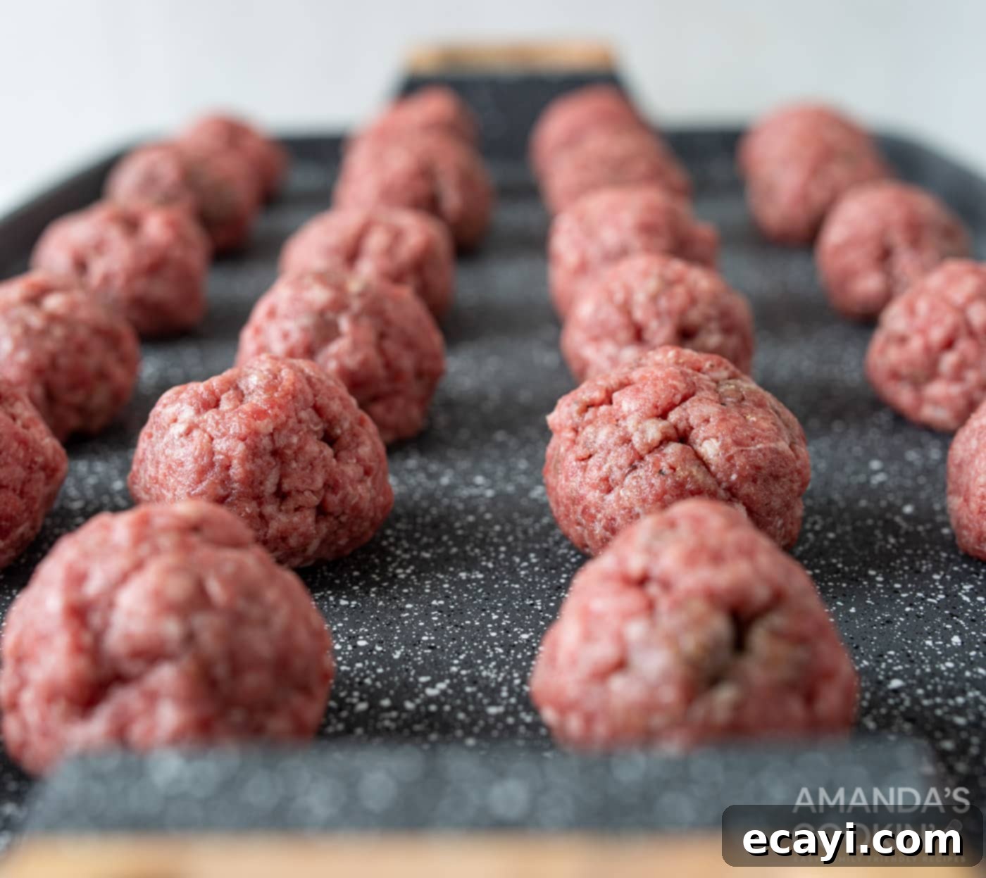 Mini Bacon Cheeseburger Poppers 6 Neatly arranged raw meatballs on a foil-lined baking sheet, prepared for baking in the oven.