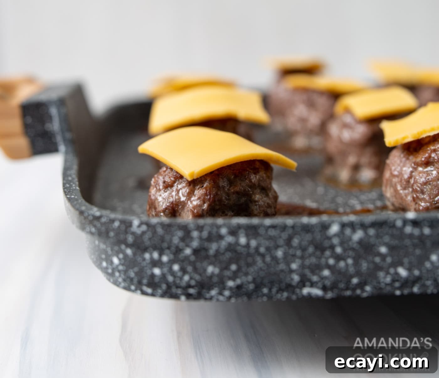 Mini Bacon Cheeseburger Poppers 8 Small, rectangular slices of American cheese artfully placed on top of freshly baked meatballs, preparing for the next layer of toppings.