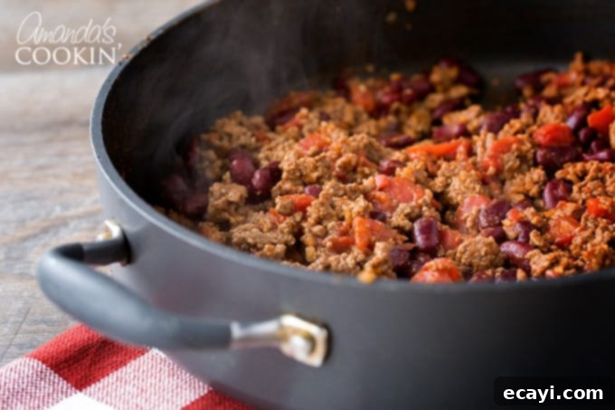 Cooking Chili Mac Base Ground beef browning in a skillet, then seasoned and mixed with beans and tomatoes, creating the chili base.