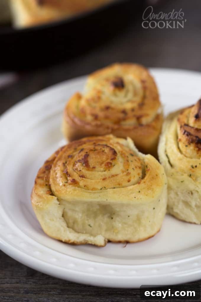 Mouthwatering Garlic Parmesan Rolls 4 A white plate holding three golden brown Parmesan garlic rolls, ready to be served.
