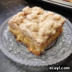 Crowd-Pleasing Crumb Cake 2 A close up photo of a square of crumb cake on a clear plate, dusted with confectioner's sugar.