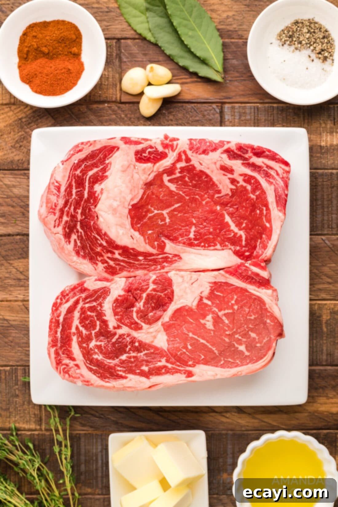 Slow-Smoked Ribeye 4 A flat lay of fresh ingredients laid out for making smoked ribeye steak, including raw ribeyes, olive oil, spices, butter, and herbs.