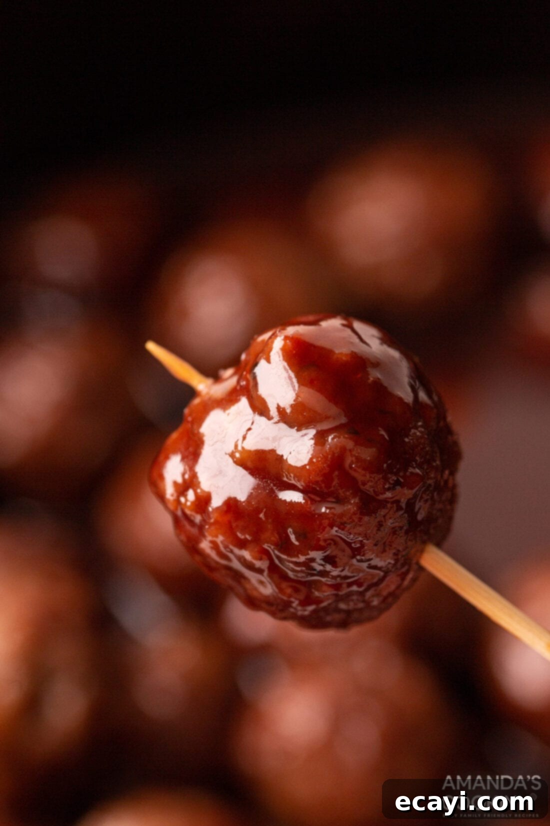 Sticky Grape Glazed Meatballs 3 Holding a delicious grape jelly meatball with a toothpick, showing its glossy, sweet and spicy coating.