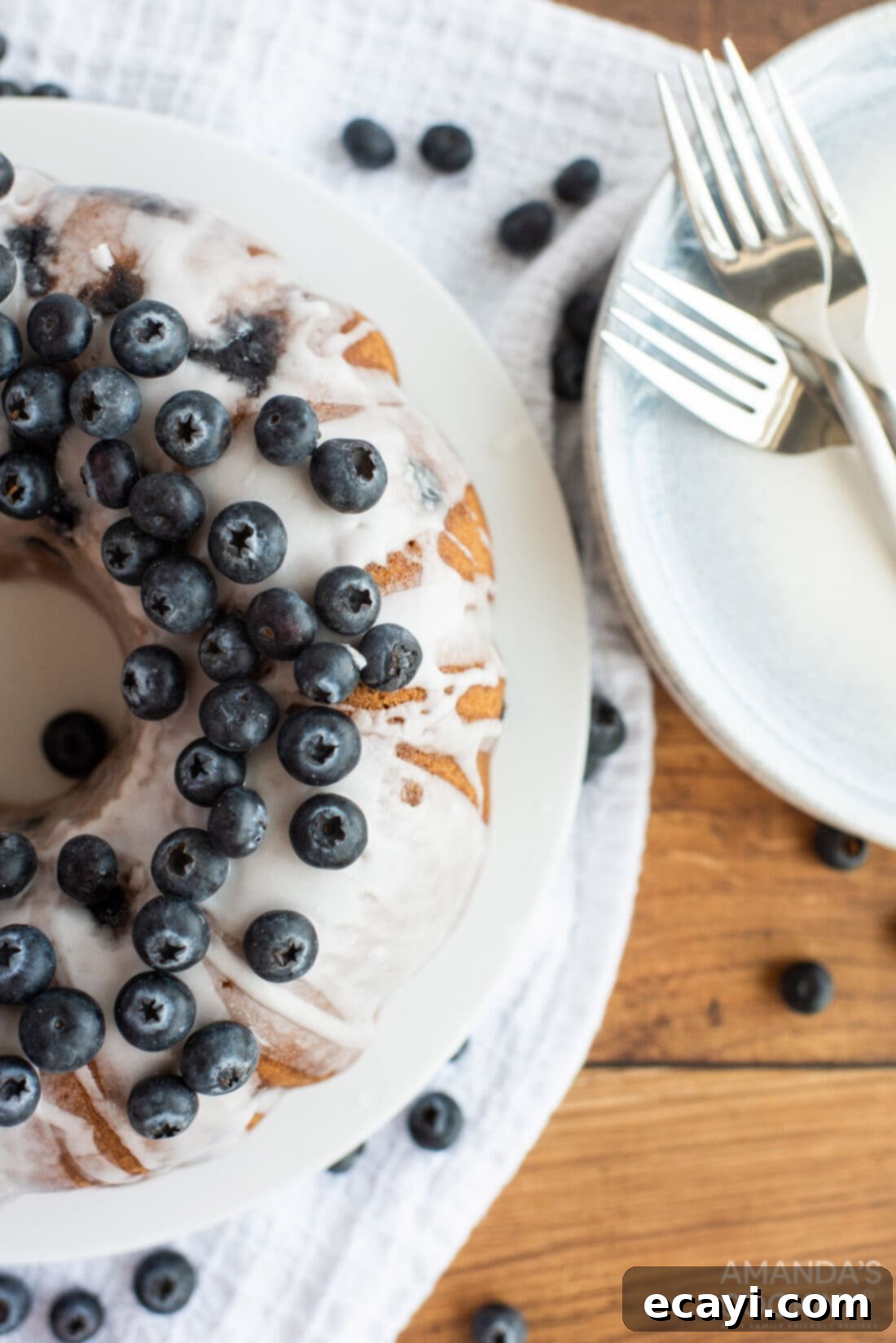 Blueberry Bliss Bundt 2 Overhead shot of a perfectly glazed Blueberry Bundt Cake with fresh blueberries scattered around