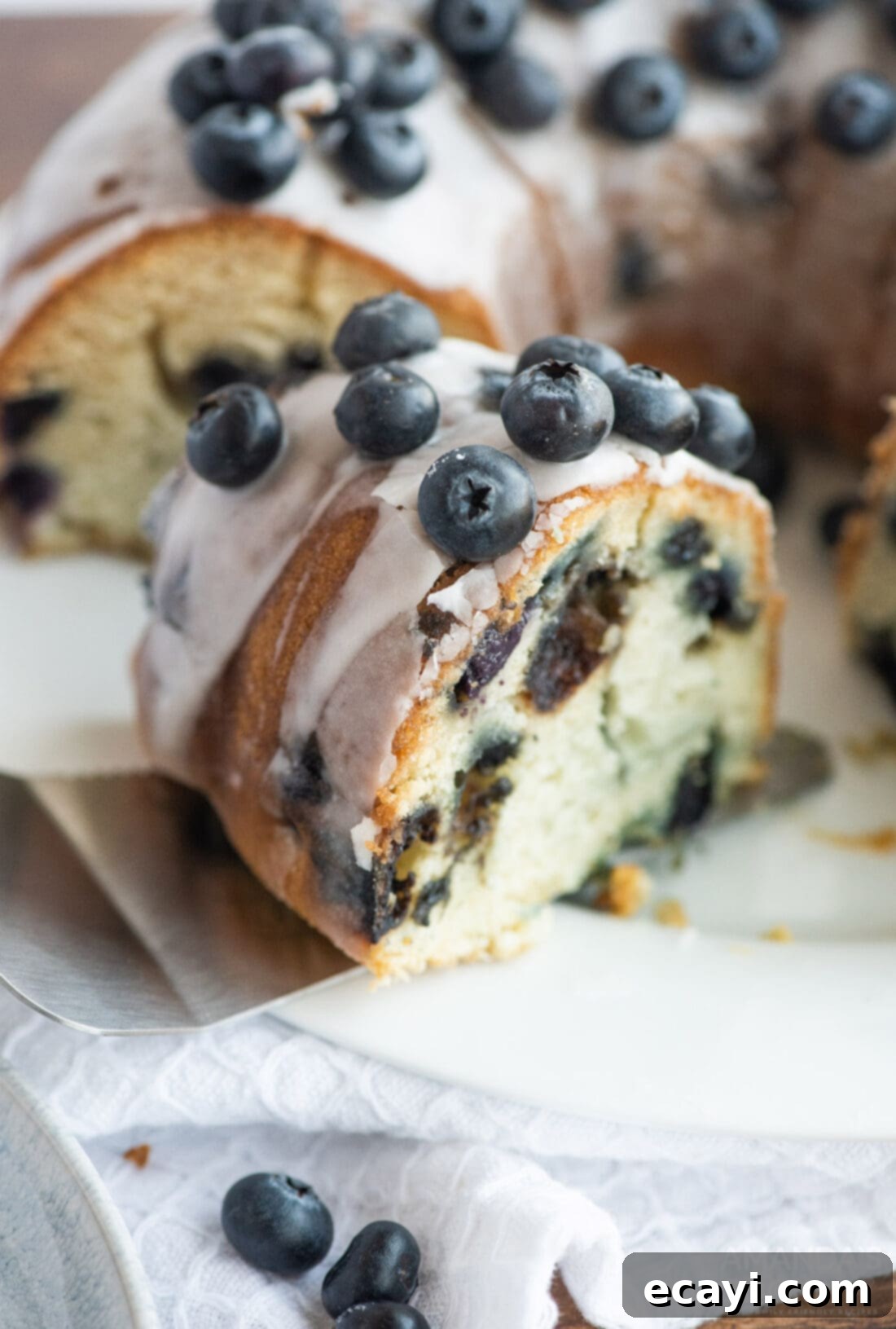 Blueberry Bliss Bundt 3 A slice being removed from a beautiful Blueberry Bundt Cake, showcasing its moist interior and blueberries